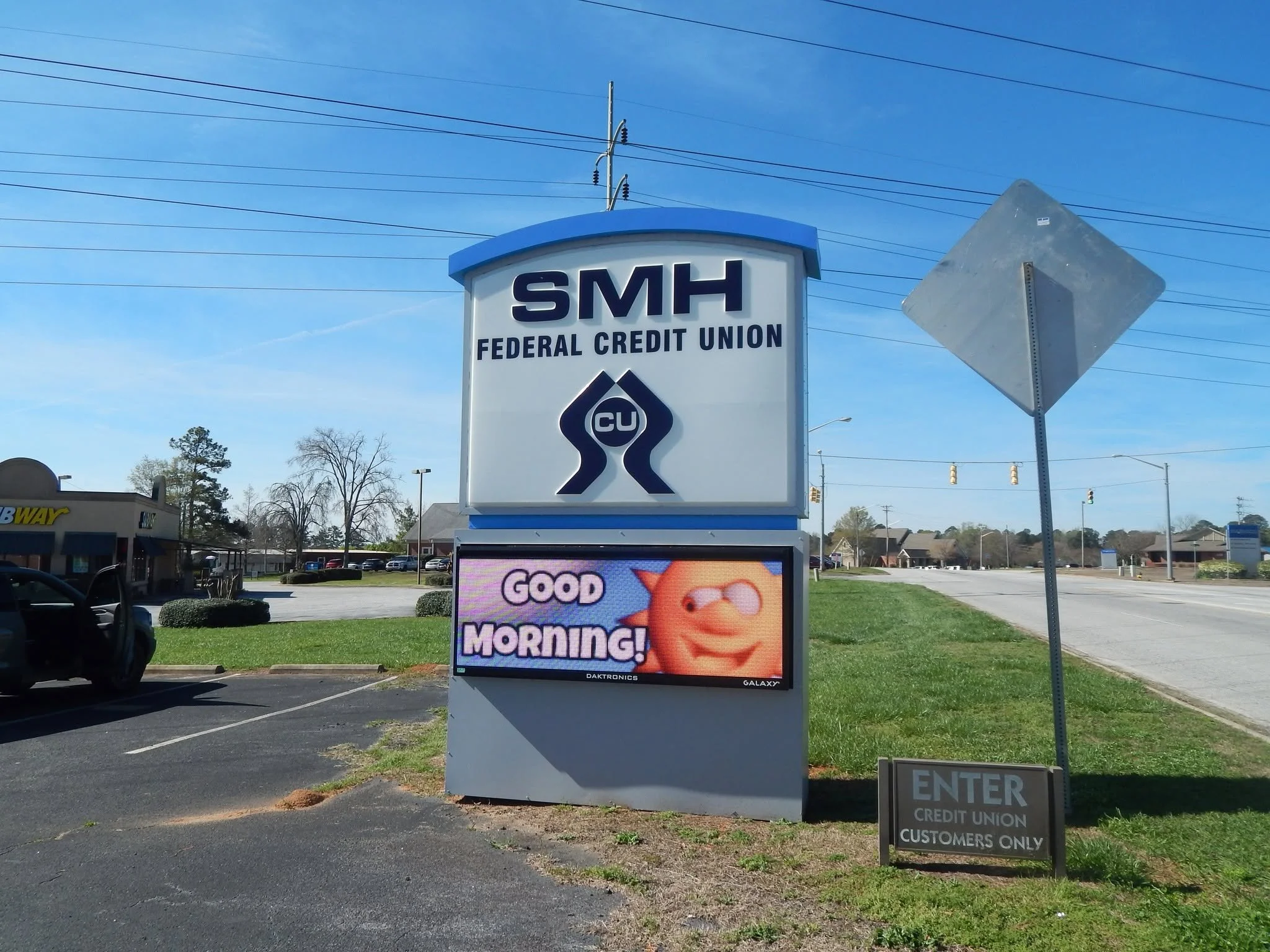 Sign for SMH Federal Credit Union with an electronic advertisement below displaying a smiley face and the message "Good Morning!" in bright colors.