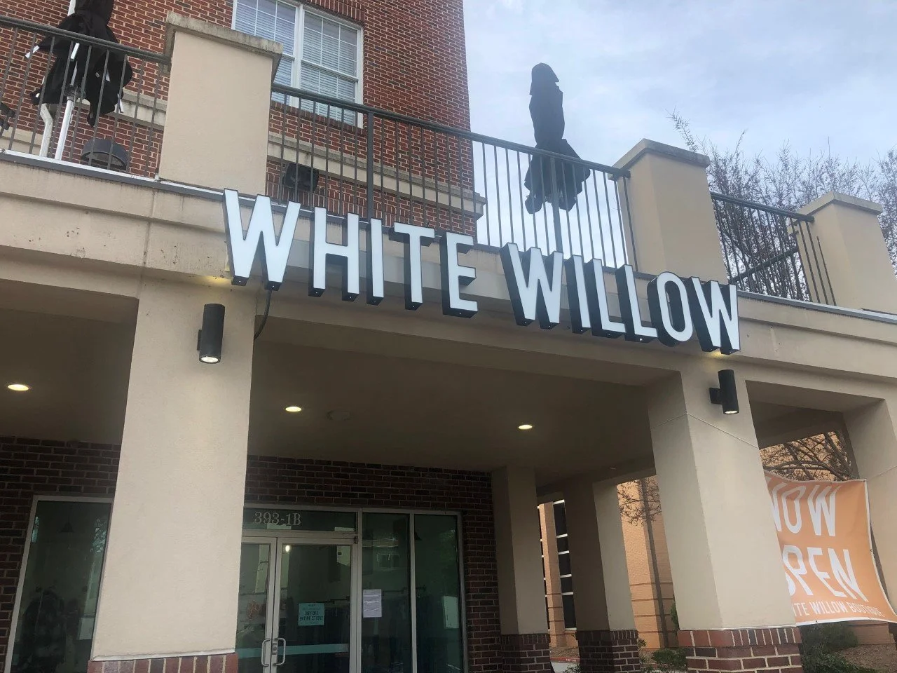 Exterior of a building with a sign that says 'White Willow' and a banner that says 'Now Open'.