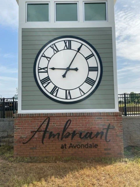 A clock tower with a large round clock face showing approximately 8:07, and a sign below that reads 'Ambrant at Avondale'.