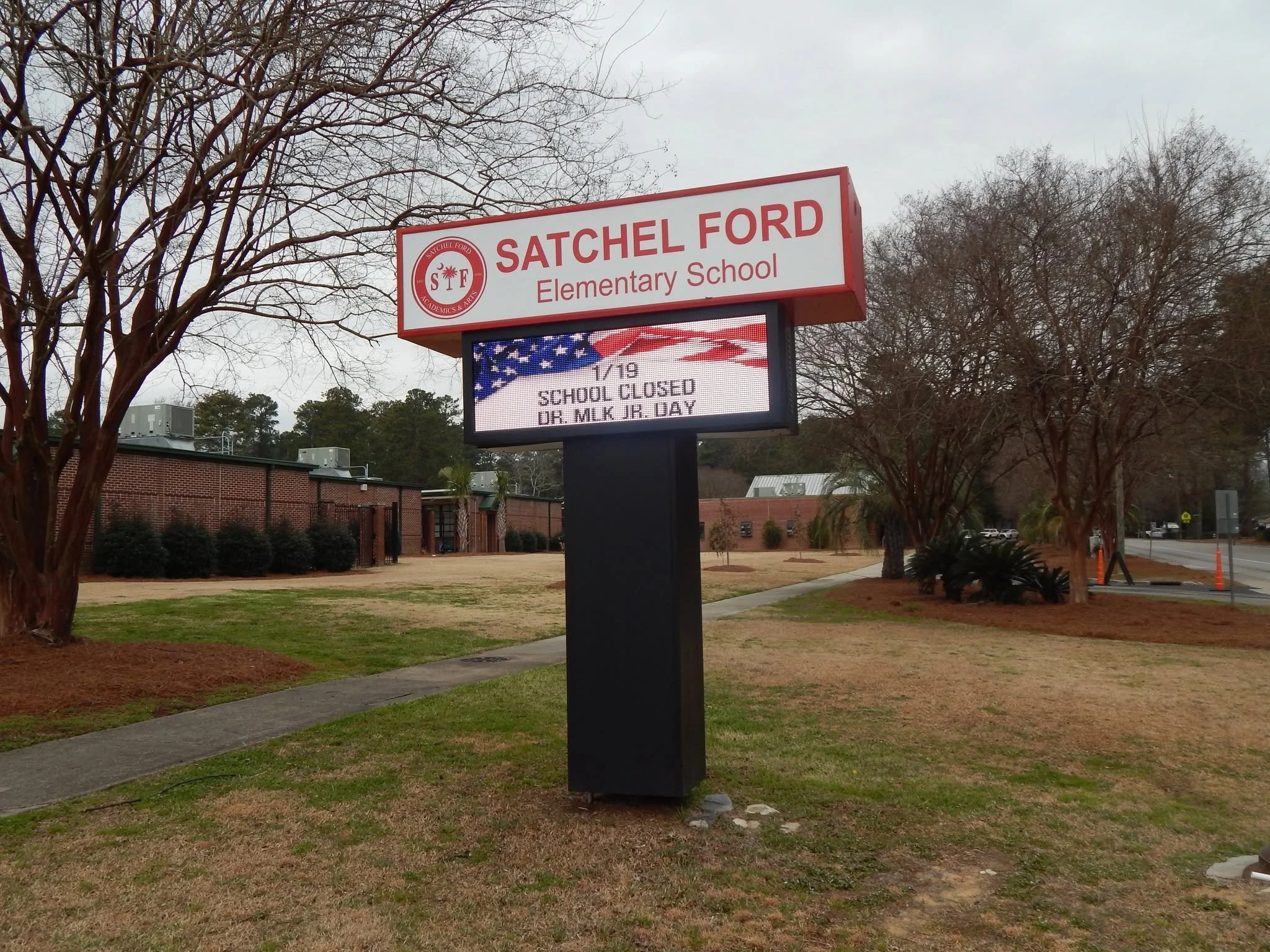 A digital sign outside Satchel Ford Elementary School announces the school is closed for Dr. Martin Luther King Jr. Day, with a graphic of an American flag.