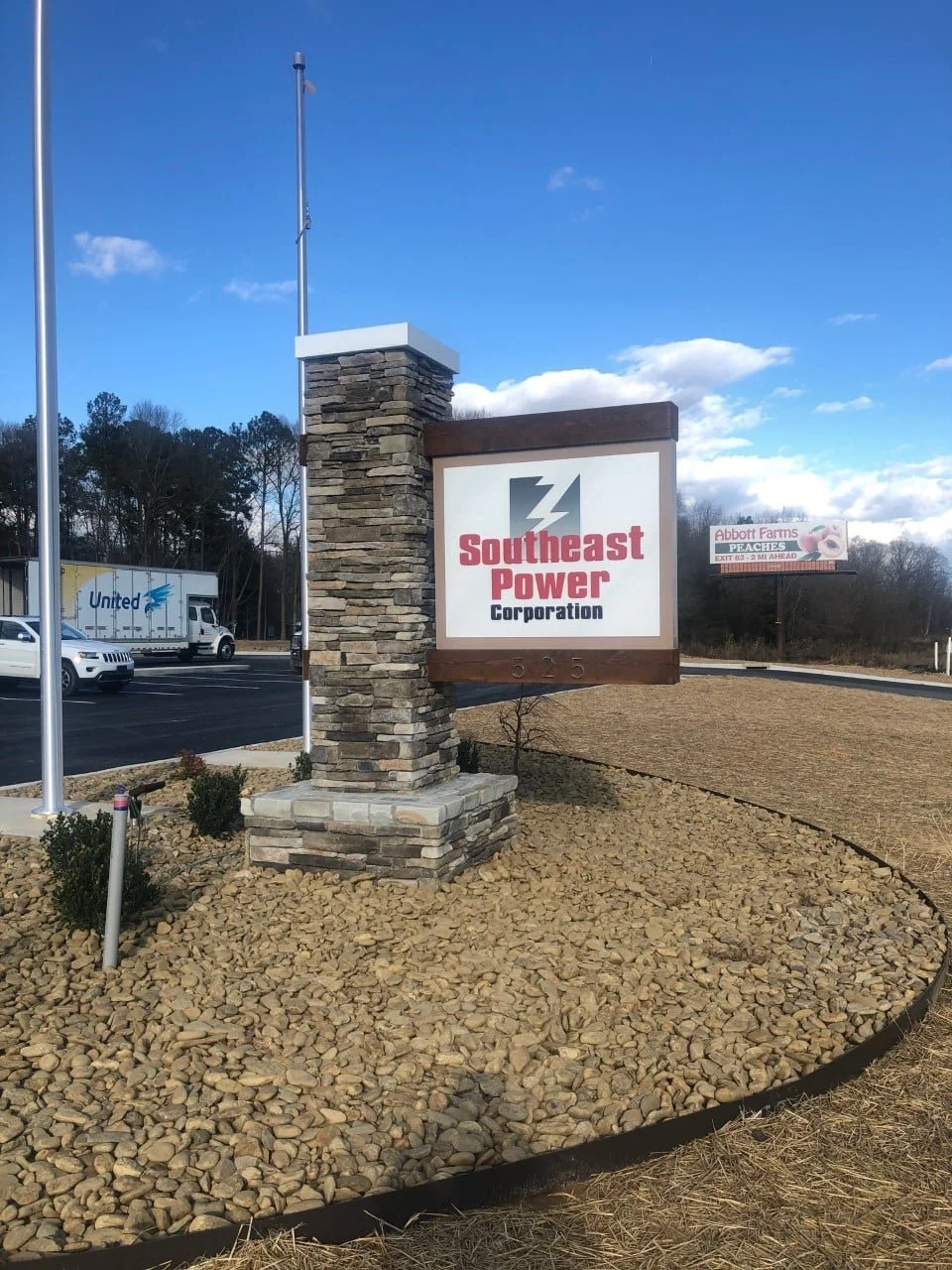 Sign for Southeast Power Corporation located near a parking lot, with a stone base and a wooden frame, against a partly cloudy sky.