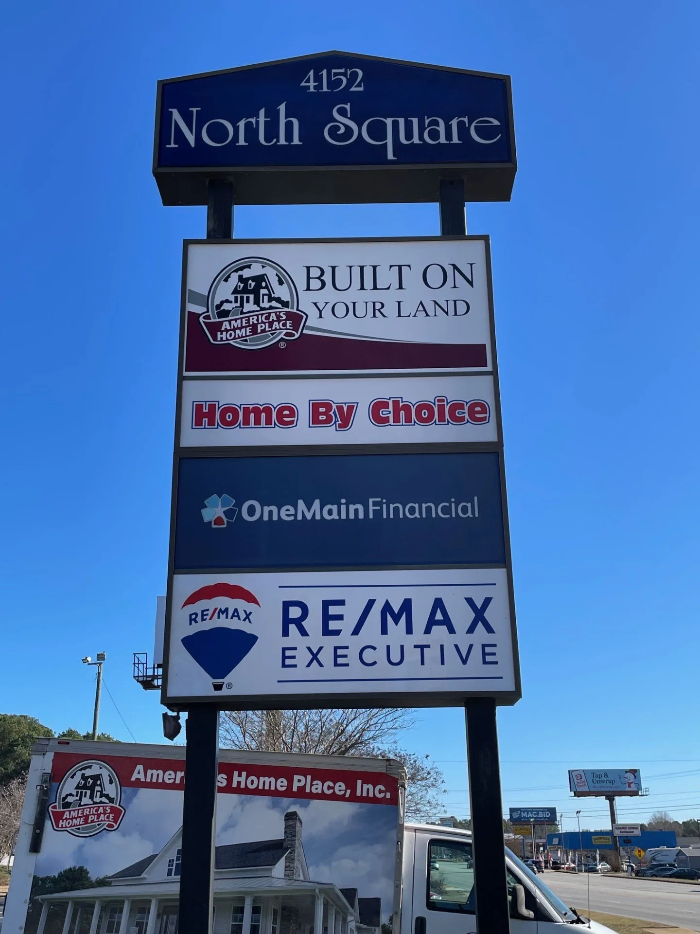 A tall sign with multiple business advertisements, topped with a blue sign displaying the address 4152 North Square.