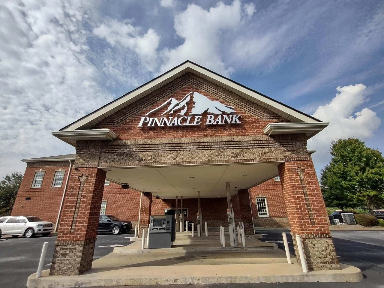Front of Pinnacle Bank building with a parking lot, cars, and a blue sky with clouds.