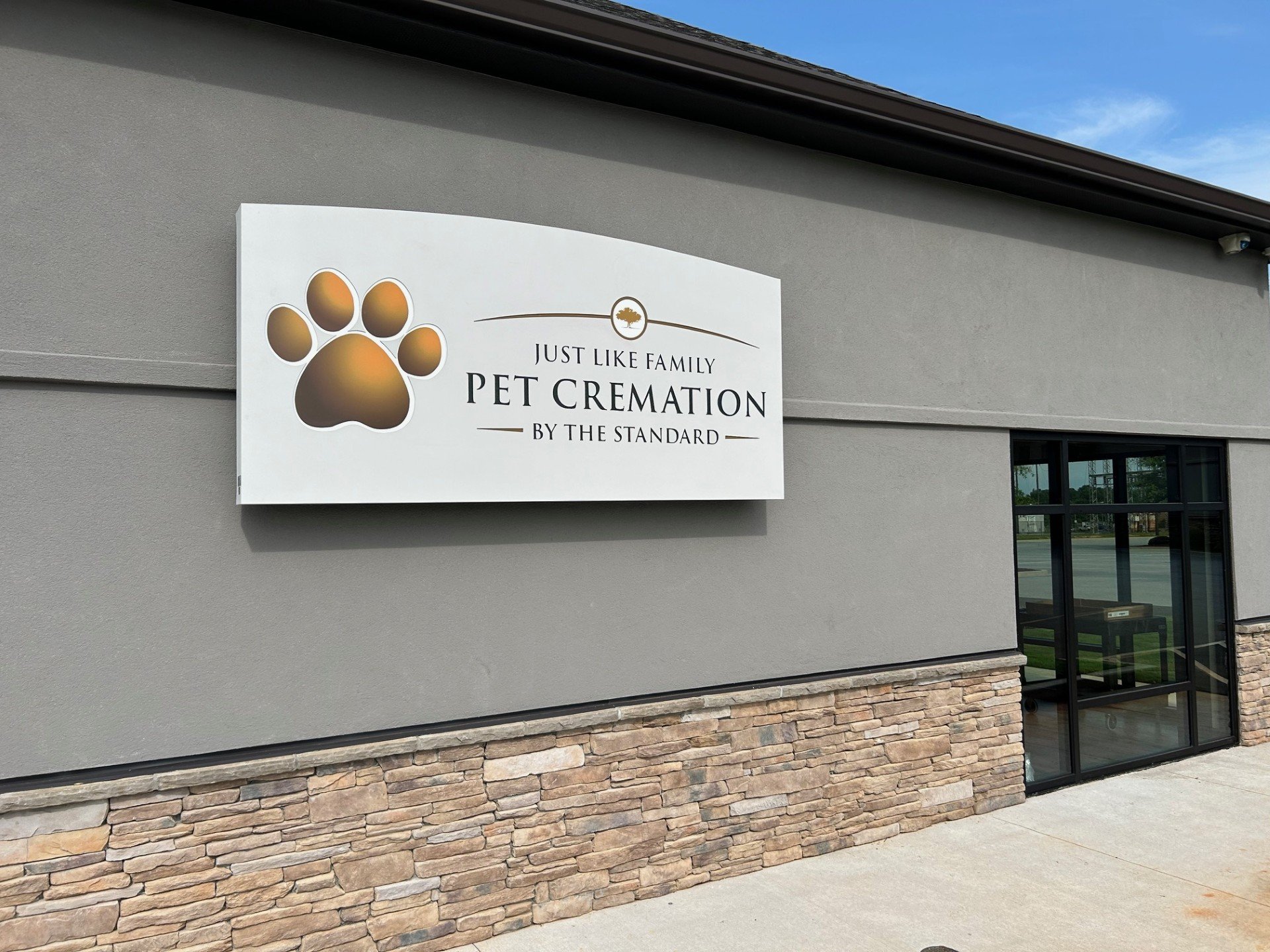 Signboard for a pet cremation service attached to a gray building wall, with a large paw print and text 'Just Like Family Pet Cremation by The Standard.'
