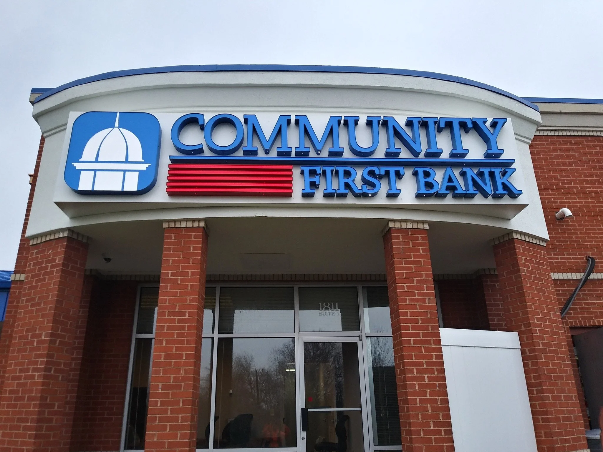 The exterior of a brick building with a sign that reads 'Community First Bank' with a logo that includes a white dome-like structure on a blue background.