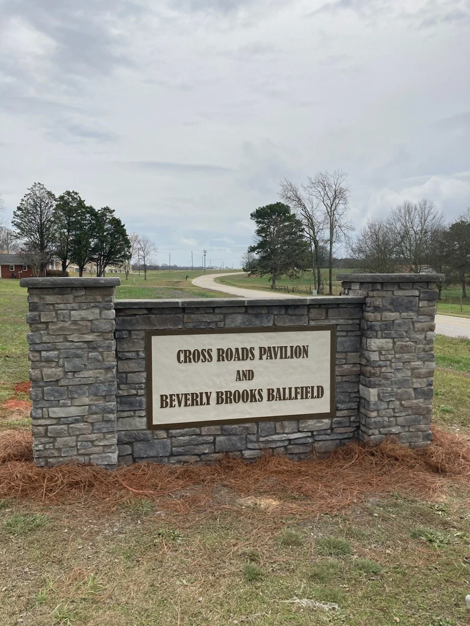 Stone sign on grass with the text 'Cross Roads Pavilion and Beverly Brooks Ballfield' in black lettering.