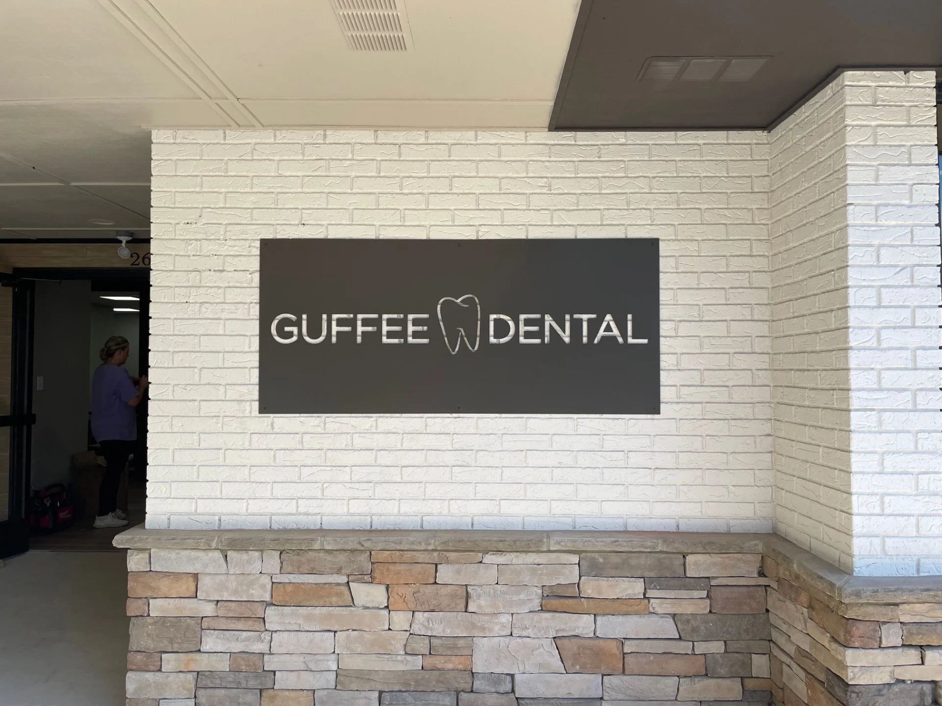 Sign on a brick wall reading 'Guffee Dental' with a tooth icon, part of a dental office exterior.