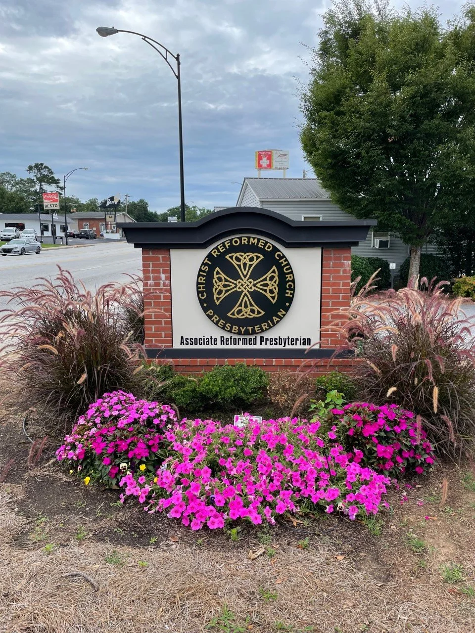 Sign for Christ Reformed Church and Associate Reformed Presbyterian surrounded by pink and purple flowers and ornamental grasses.