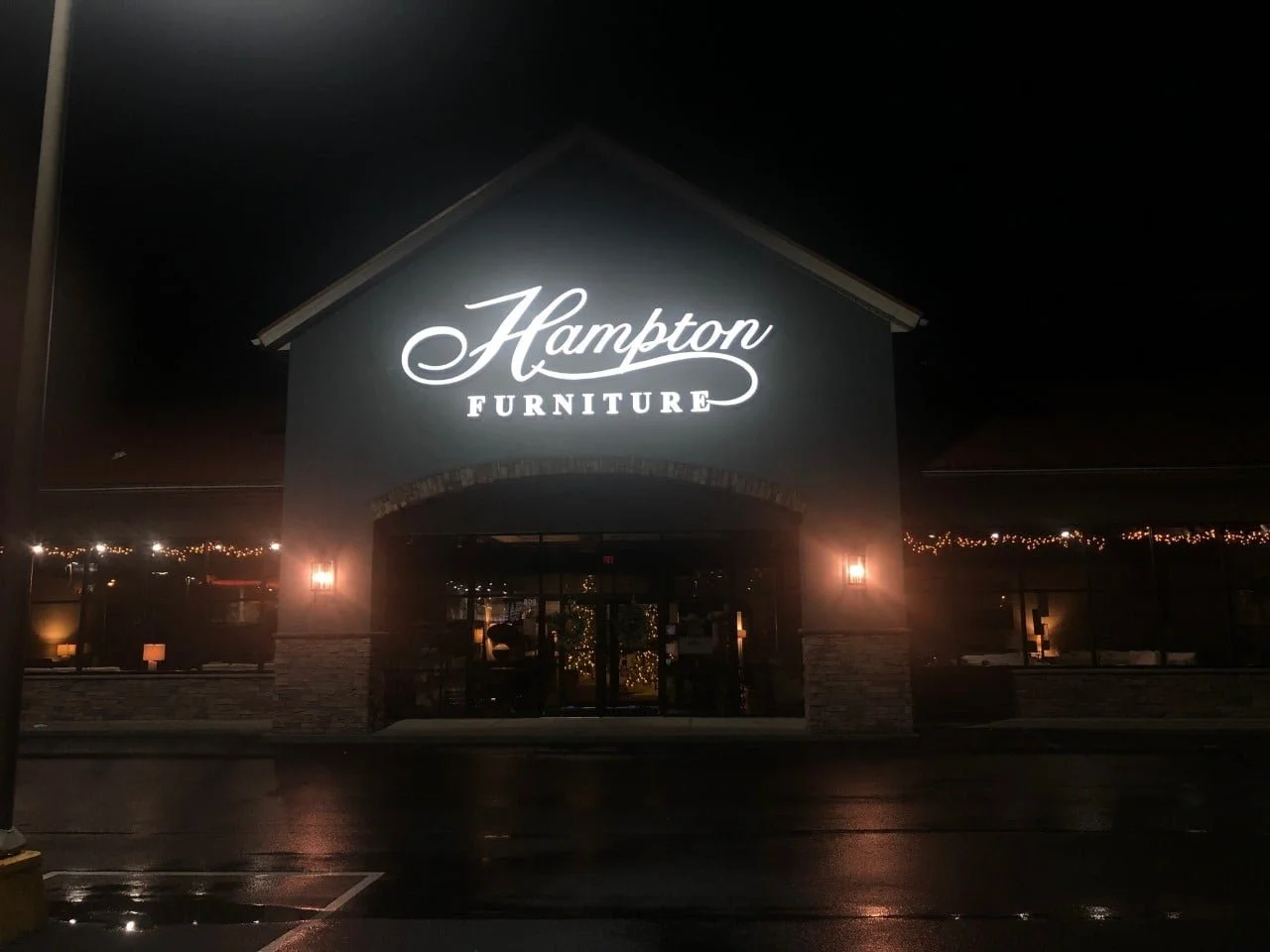 Night view of Hampton Furniture store with illuminated sign, dark sky, and reflections on wet pavement