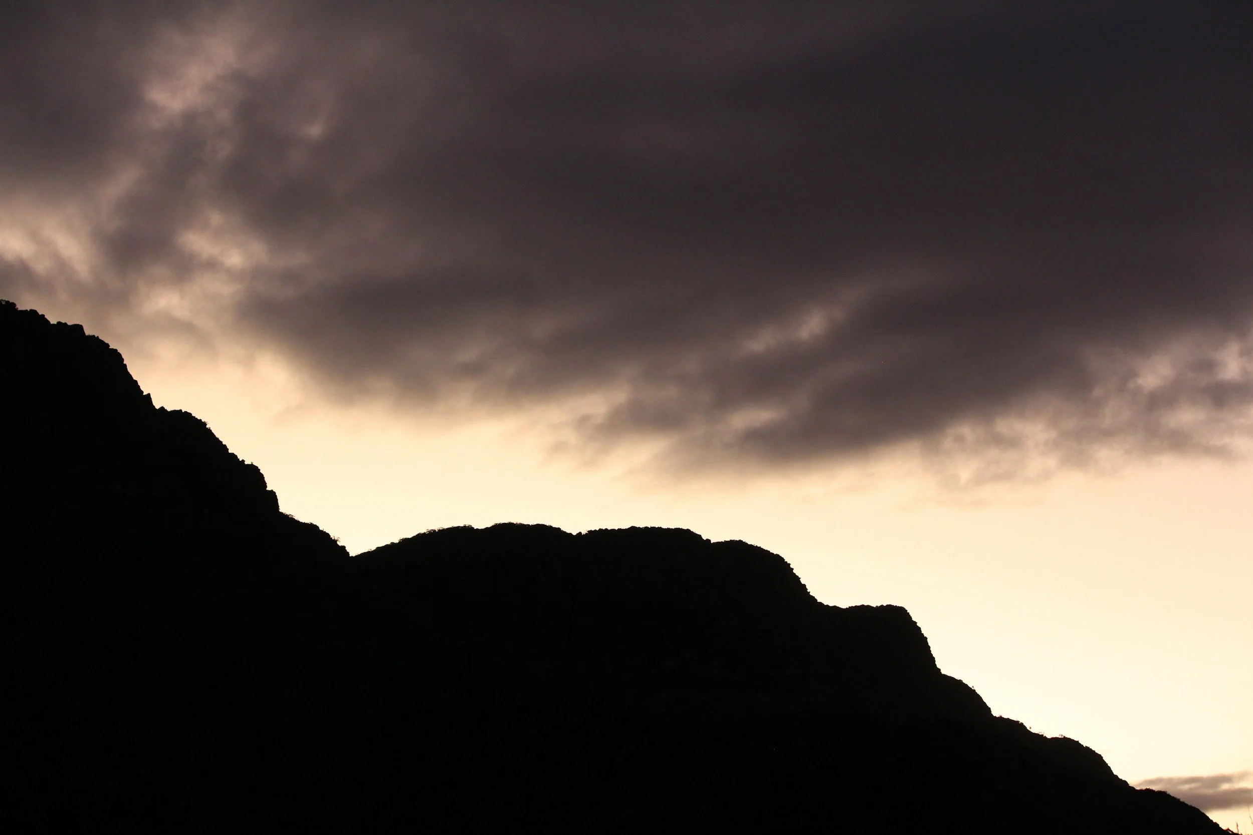 Dark clouds over mountain silhouettes at sunset or sunrise.