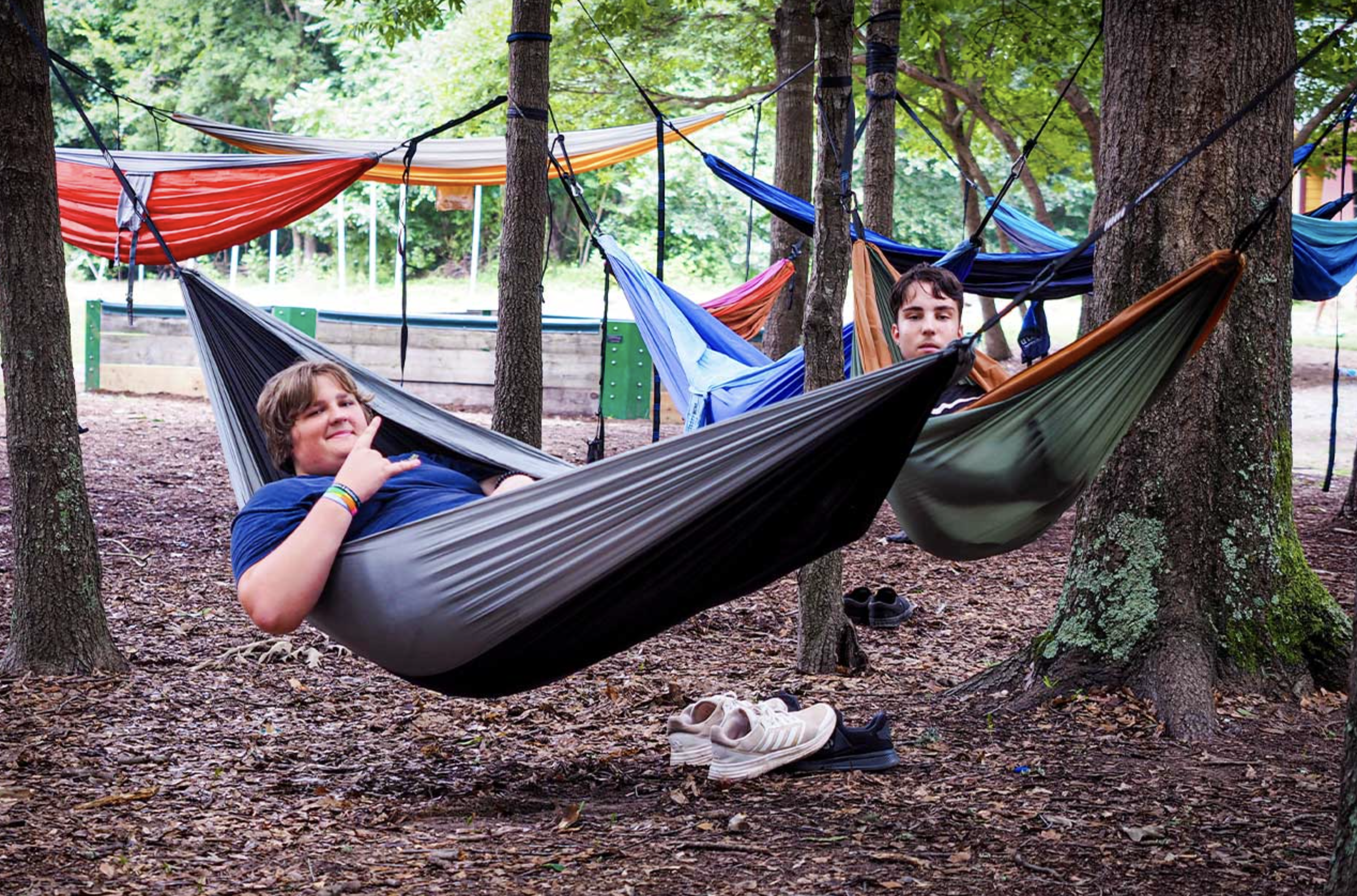 Two boys are relaxing in hammocks tied between trees in a wooded area at Riverstone at Canaan.