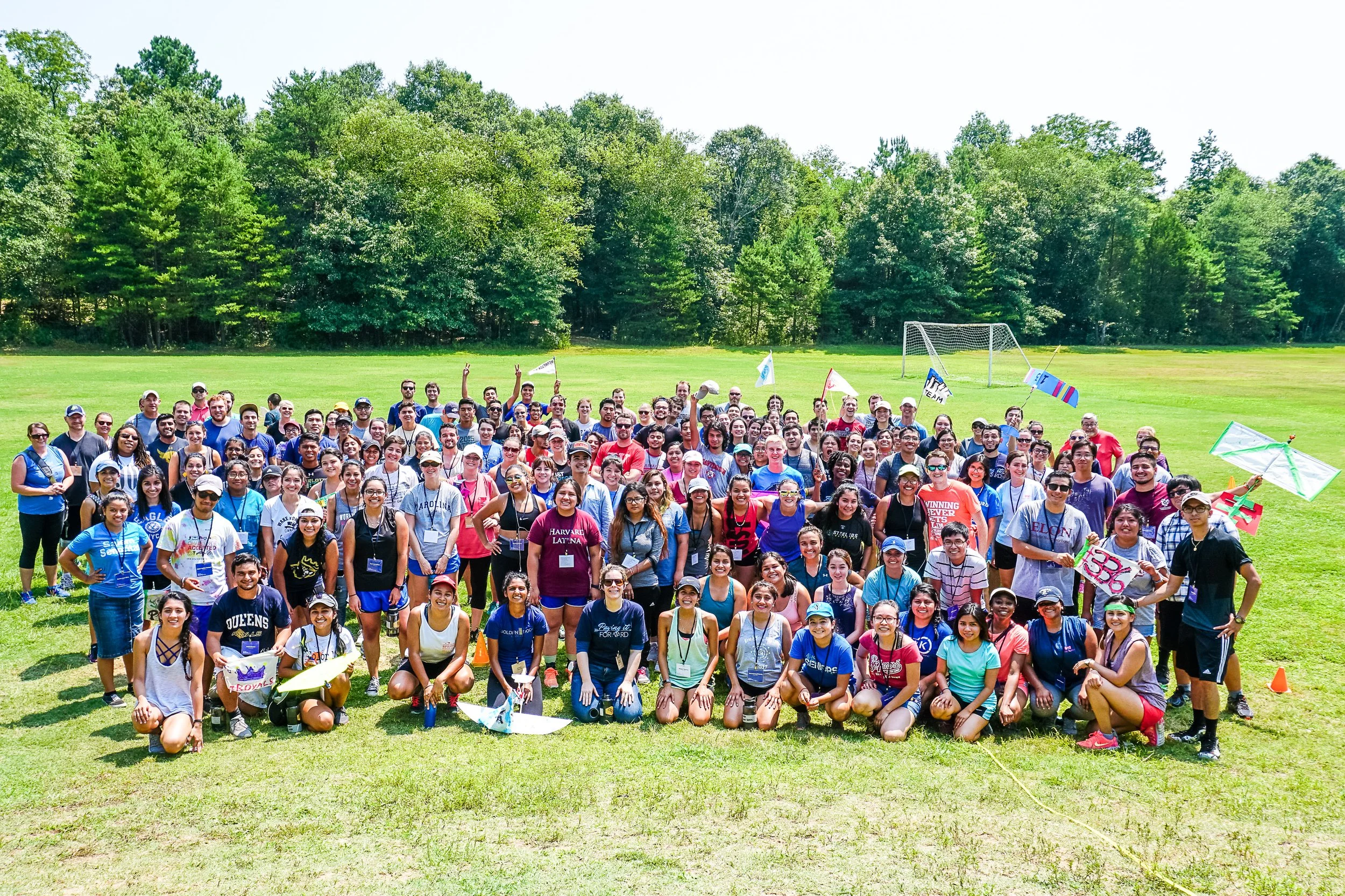 Large group of people gathered outdoors on a grassy field, posing for a group photo with trees in the background at Riverstone at Canaan.