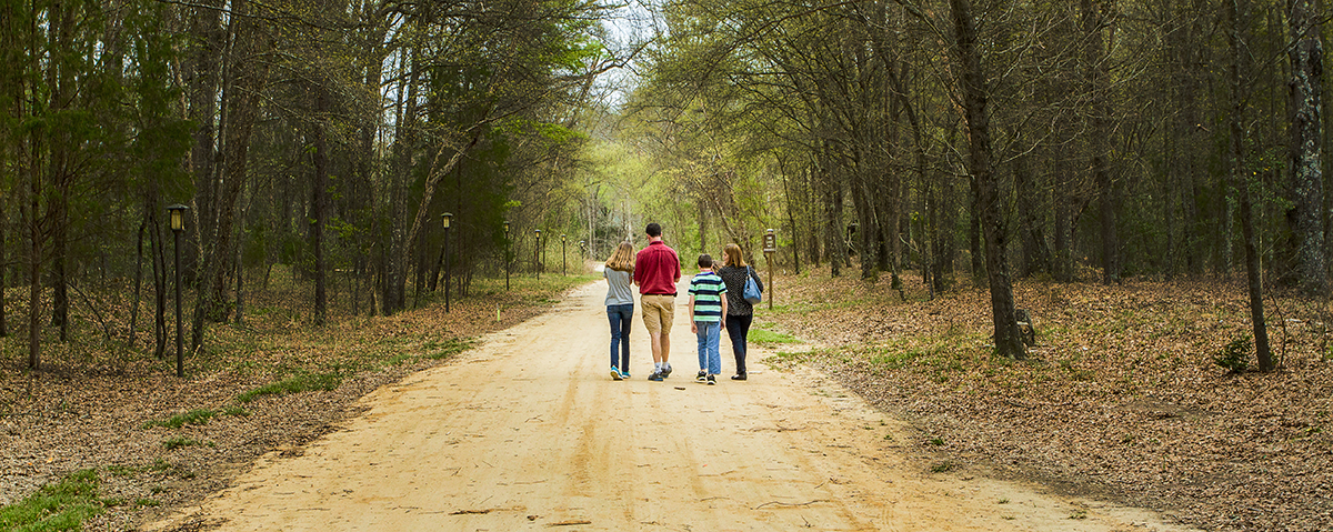 A family of four walking on a dirt path through a wooded park on a spring day at Riverstone at Canaan.