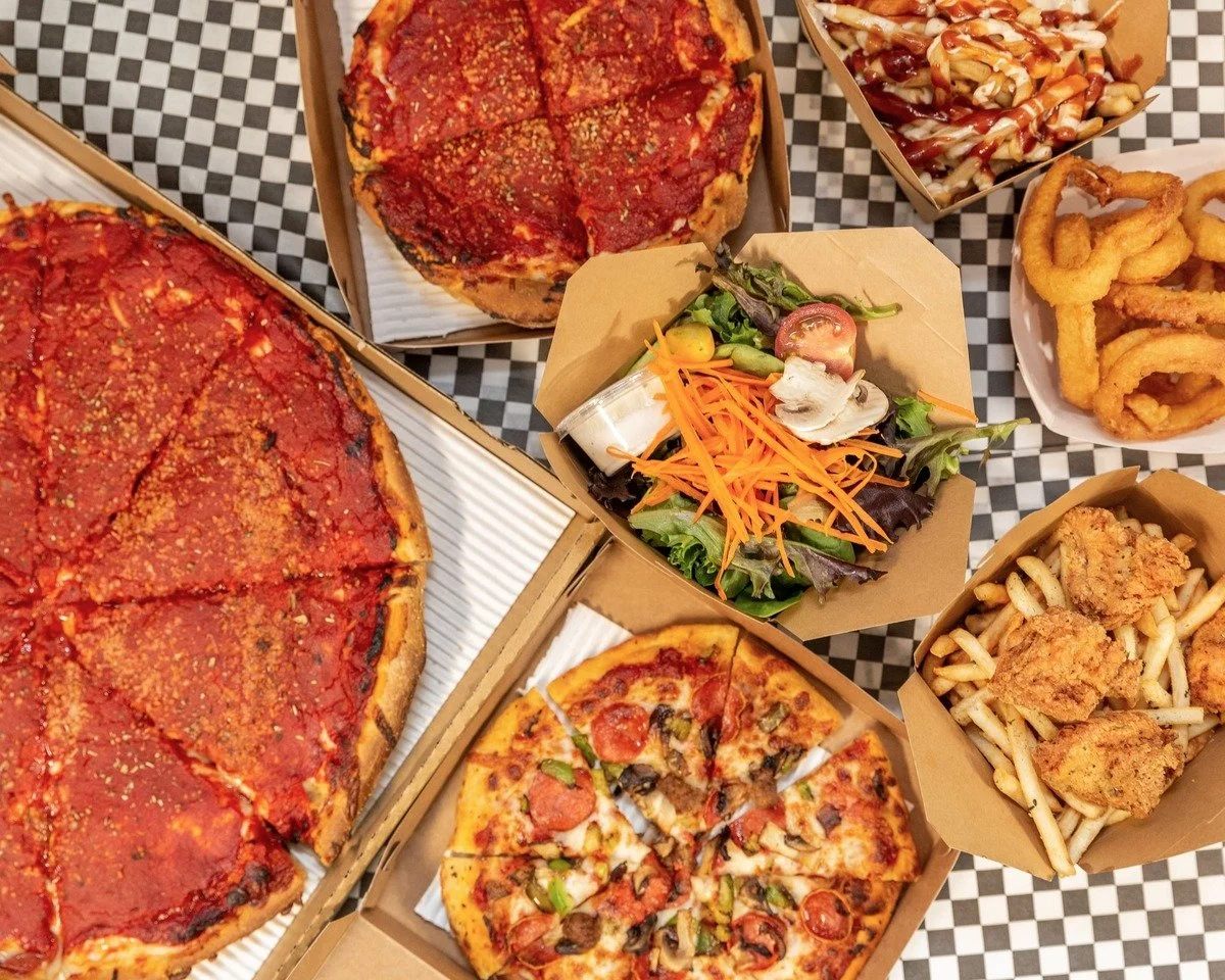 Various pizza slices, a side salad, onion rings, crispy chicken tenders with fries, and pasta with sauce on a checkered tablecloth.