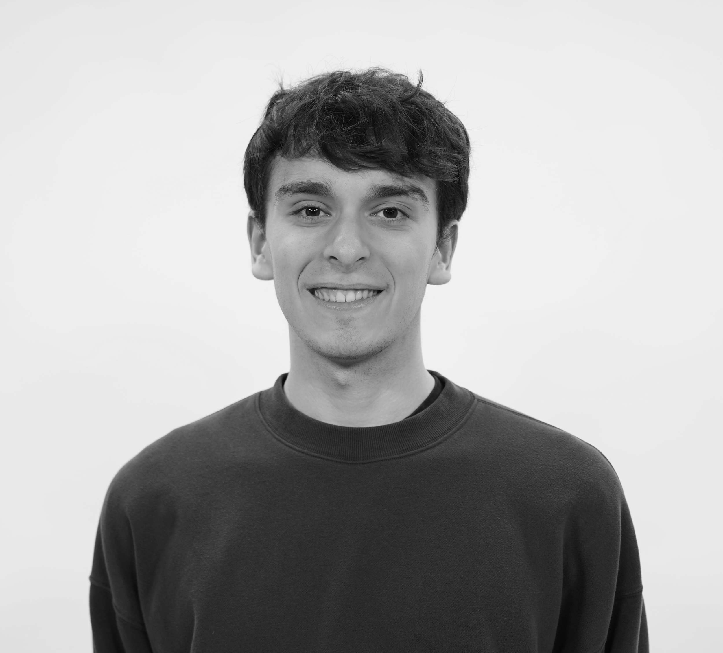 Black and white photograph of a young man with short, tousled hair, smiling, wearing a dark crew neck shirt.
