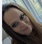 A close-up selfie of a woman with light brown hair, dark eyeliner, and subtle makeup, in front of a window with blinds.