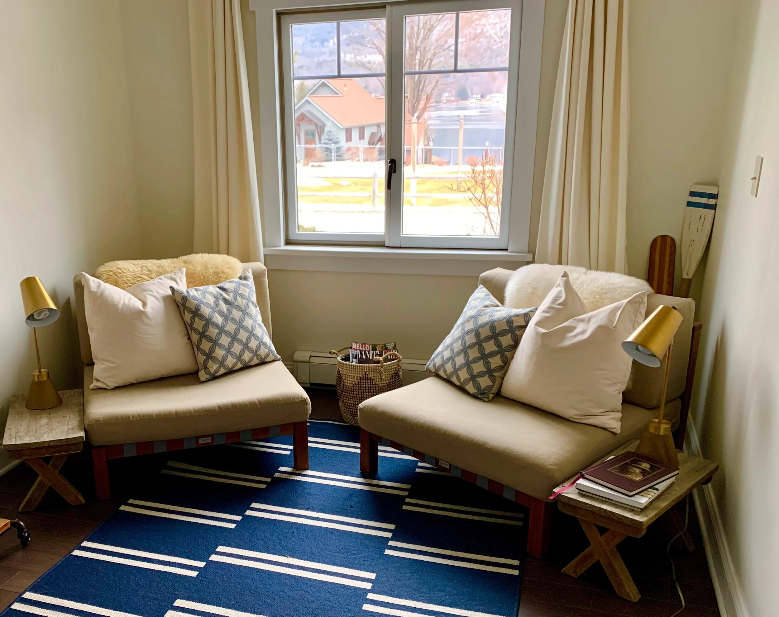A bedroom with a white bed, blue curtains, framed pictures, black nightstands with lamps, and sliding glass doors leading outside to greenery.