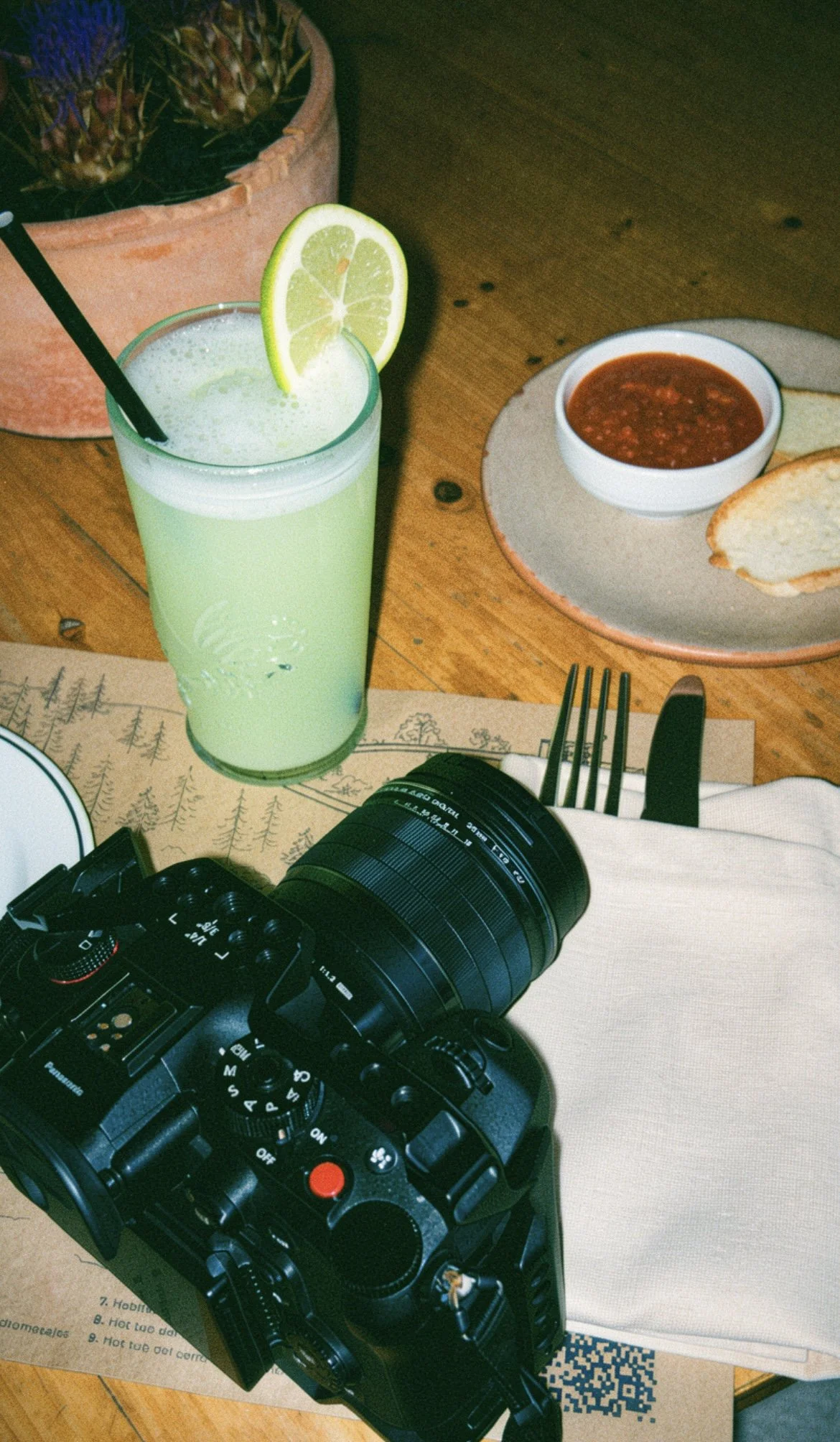 Verre de jus de citron vert avec une tranche de citron vert sur le rebord, à côté d'une assiette avec de la sauce tomate et du pain.