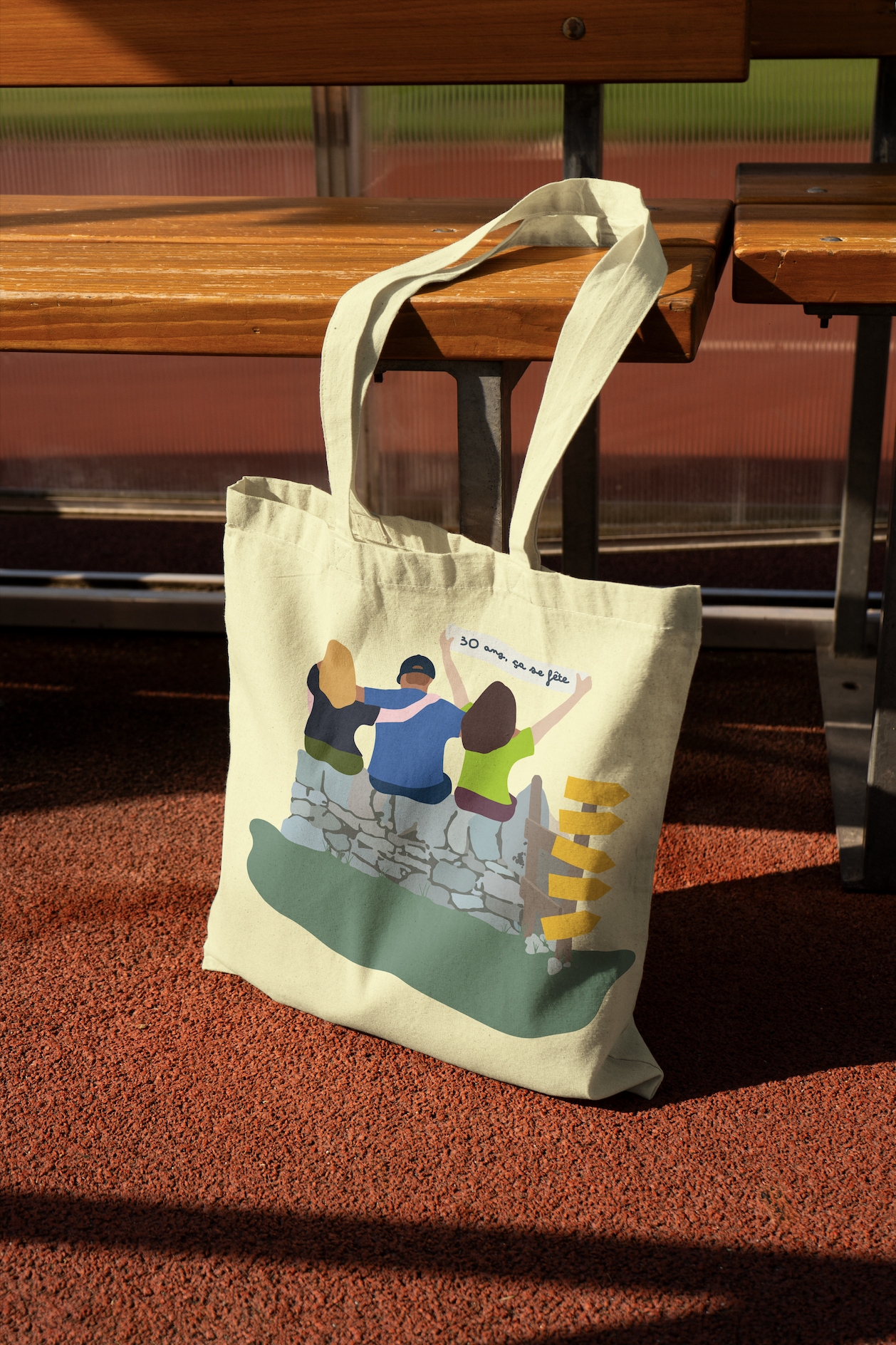 Sac en coton beige avec illustration de trois personnes assises sur un mur avec un panneau indicateur, devant un banc en bois.