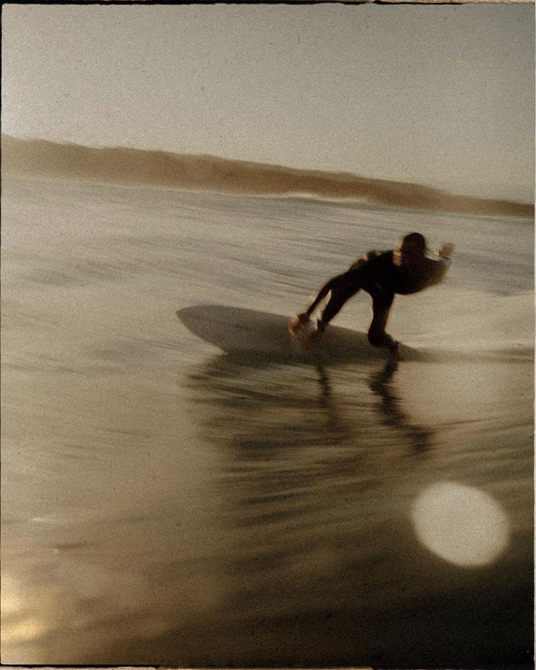 A person surfing on a wave at night or in low light, with a blurred background and their shadow visible on the sand or water.