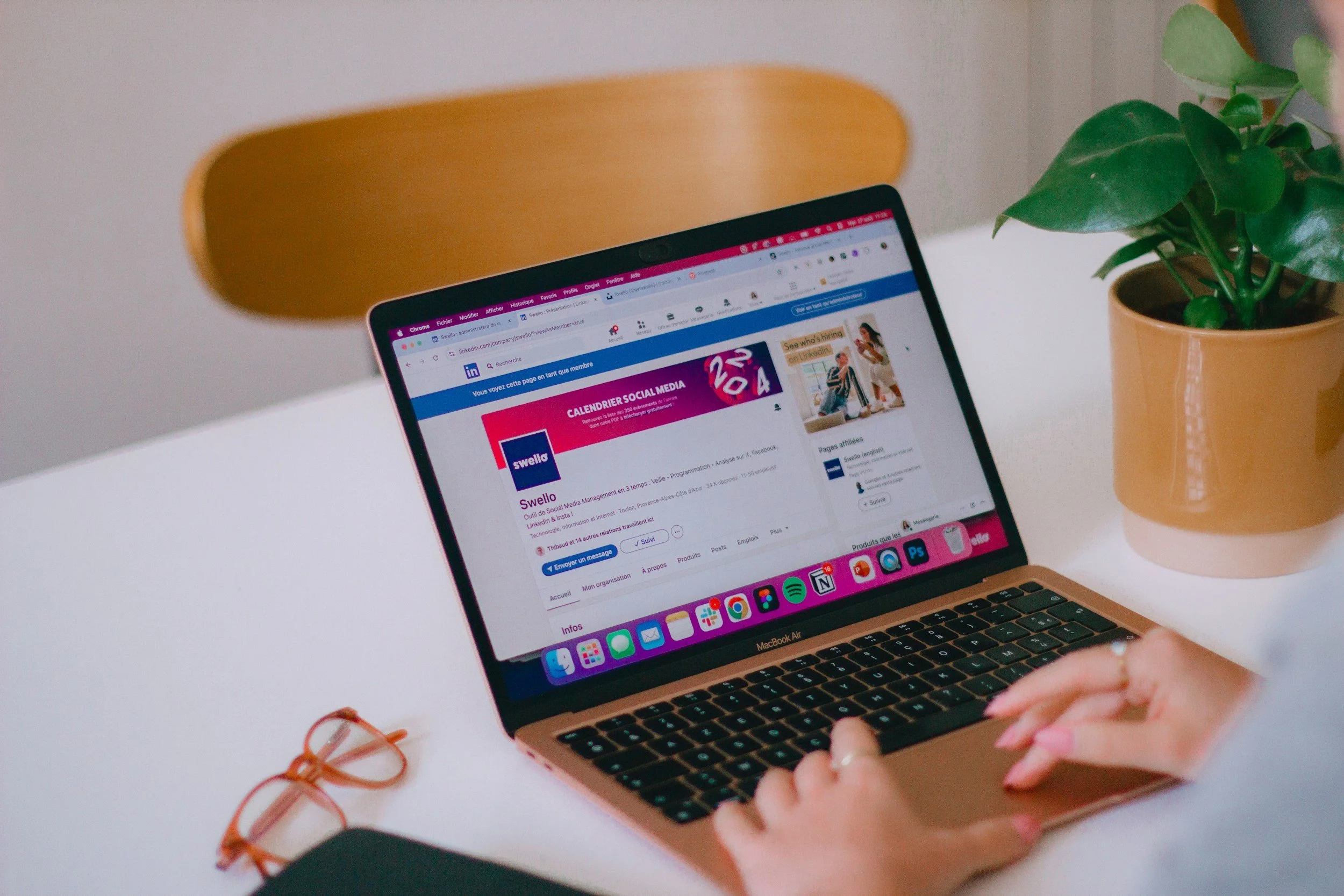 A person using a MacBook Air laptop to view a LinkedIn page on social media, with green potted plant nearby on a white desk.