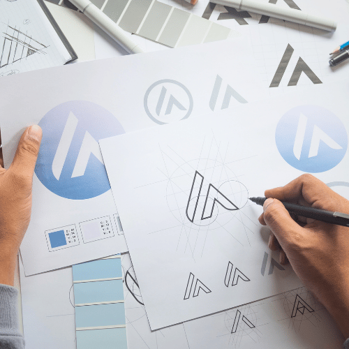 Person sketching a logo design on paper with various logo sketches and color swatches around.