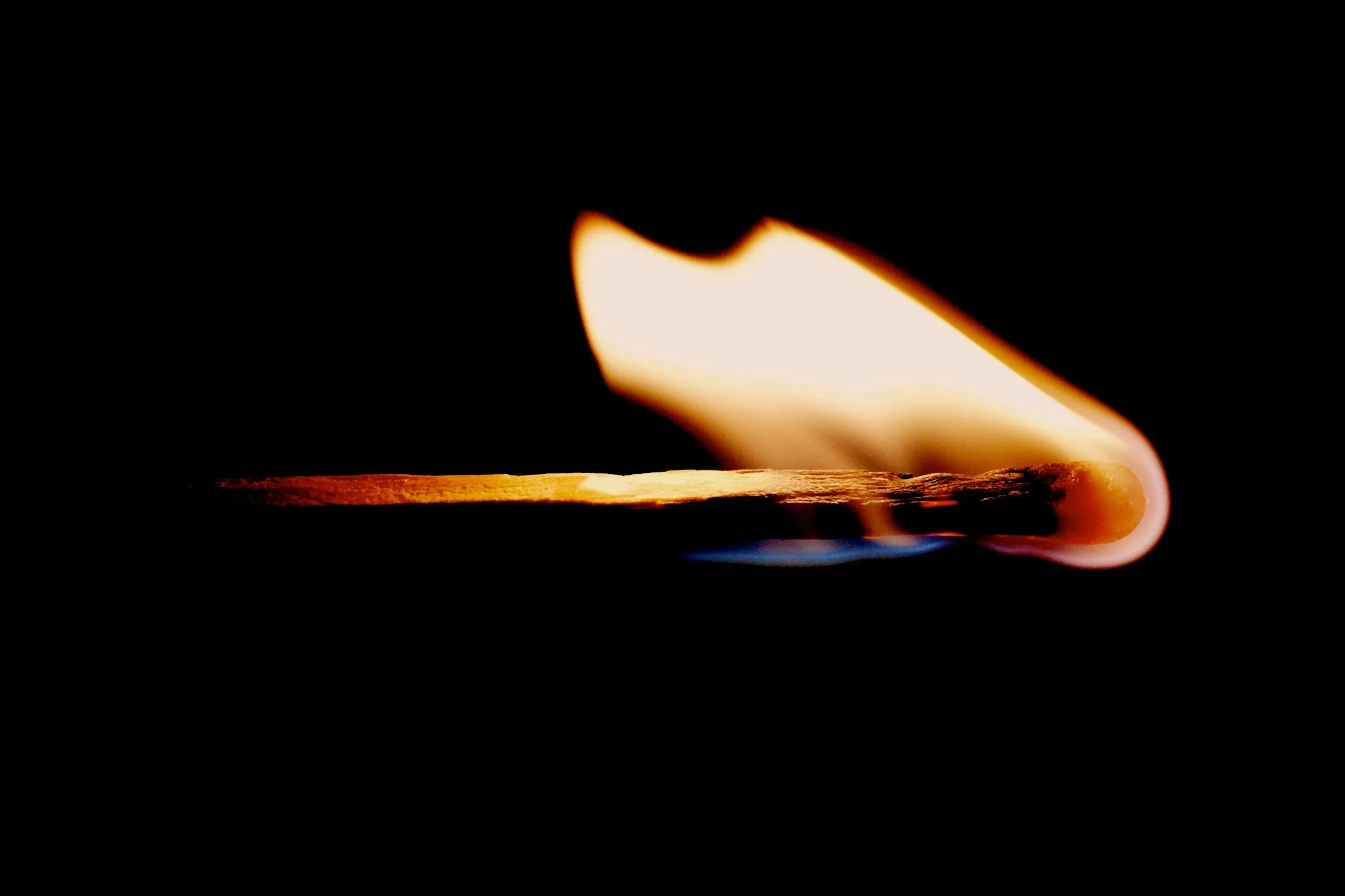 Close-up of a lit match head with a burning flame on a black background.