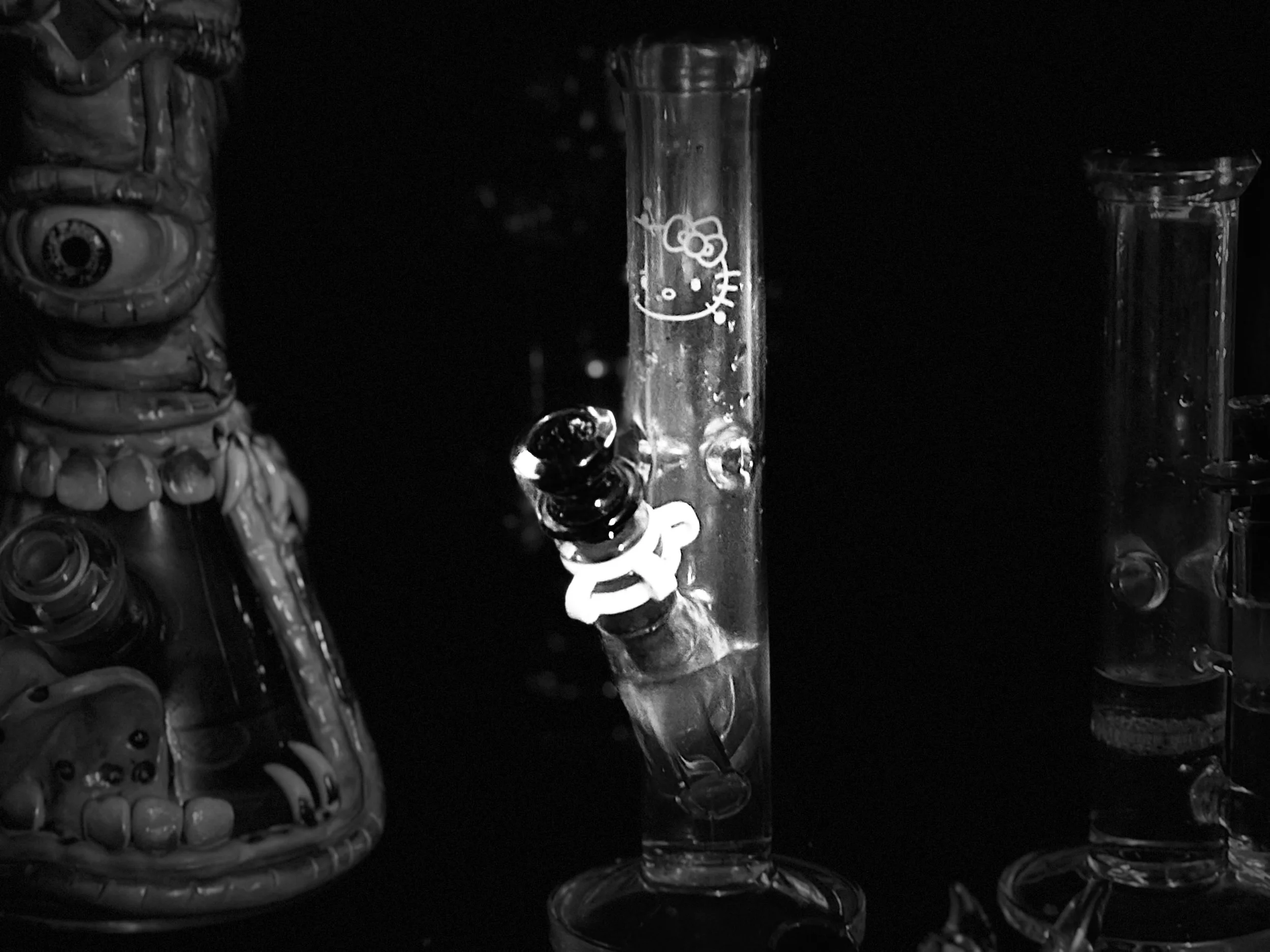 Black and white photograph features several glass test tubes, one of which has a Hello Kitty character design on it, surrounded by various cylindrical and rounded objects.