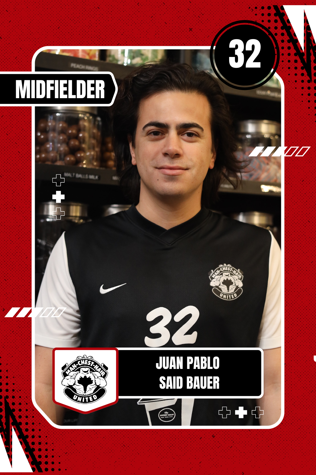 A young man with dark, wavy hair wearing a black and white Manchester United soccer jersey with the number 32, standing in front of shelves filled with jars of candies or snacks in a store.