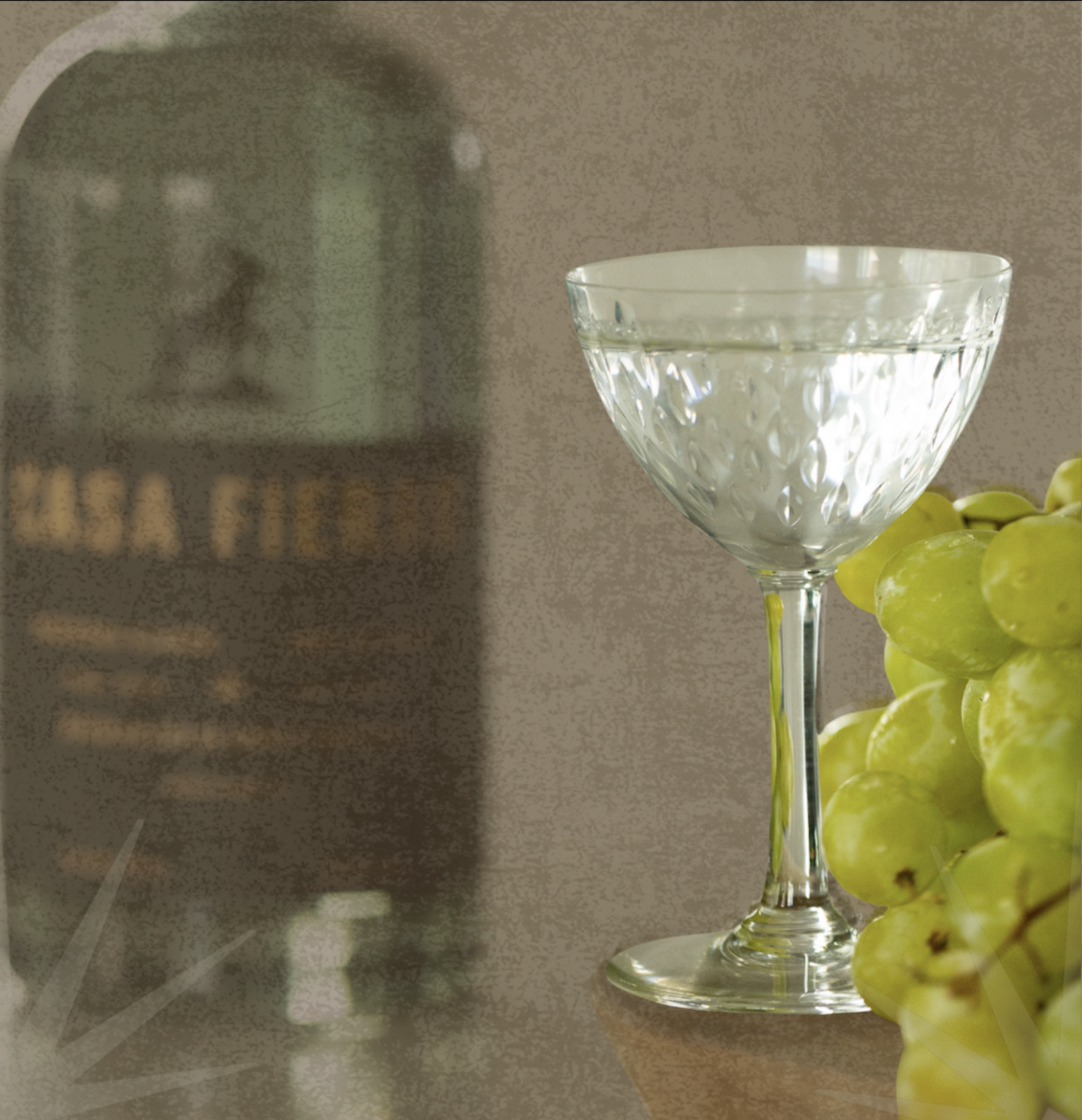 Close-up of a small martini glass with clear liquid with a bunch of frozen green table grapes, with Dark green grey bottle Casa Fierro Agave Spirit Bacanora Blanco Tequila Mezcal black label and copper colored label