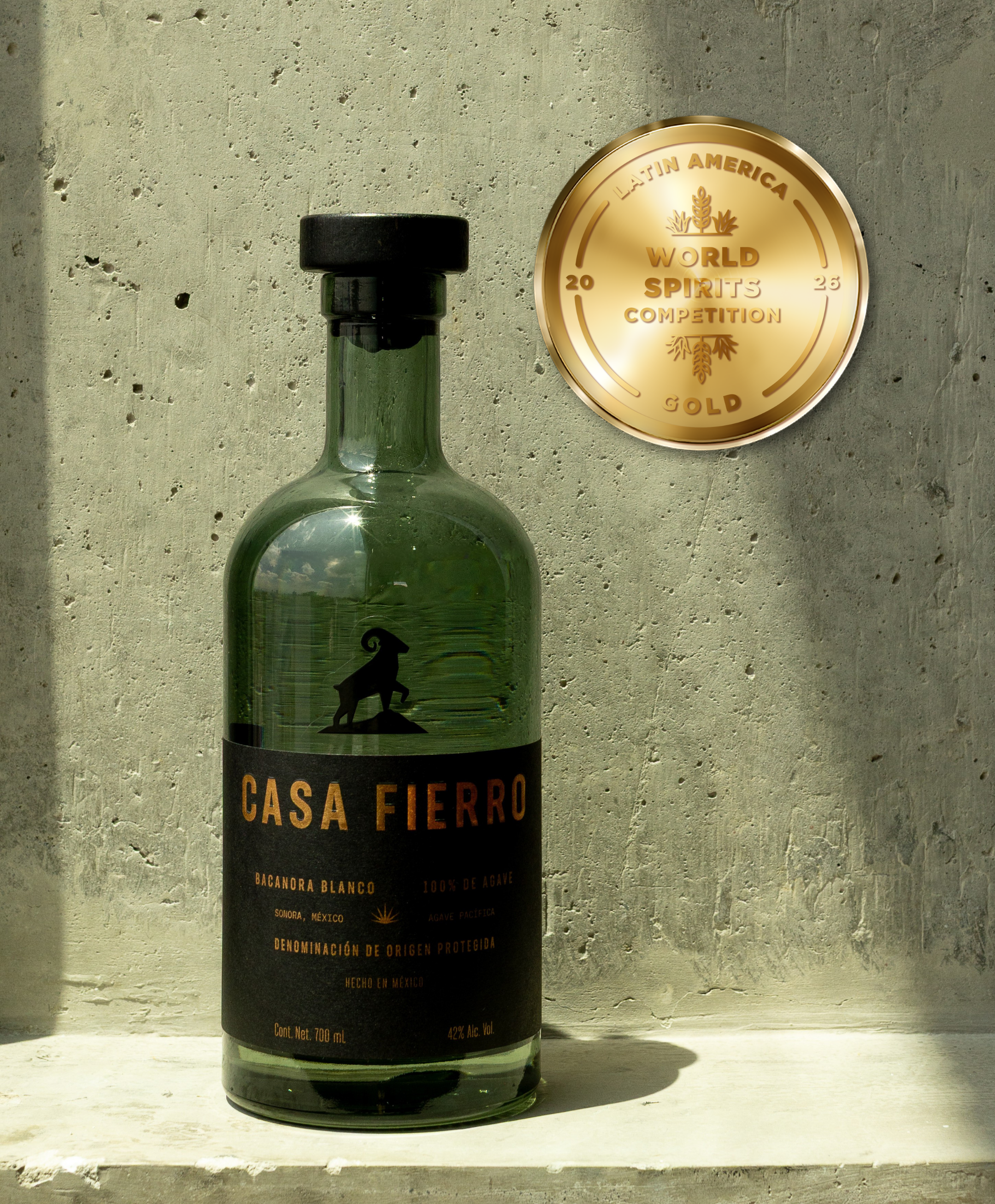 Dark green grey smoky bottle Casa Fierro Bacanora Blanco Tequila Mezcal 100% Agave Spirit black silhouette of bighorn sheep. A gold medal plaque Latin America World Spirits Competition 2026 to the right of the bottle.  Tasting Alliance.  Sonora
