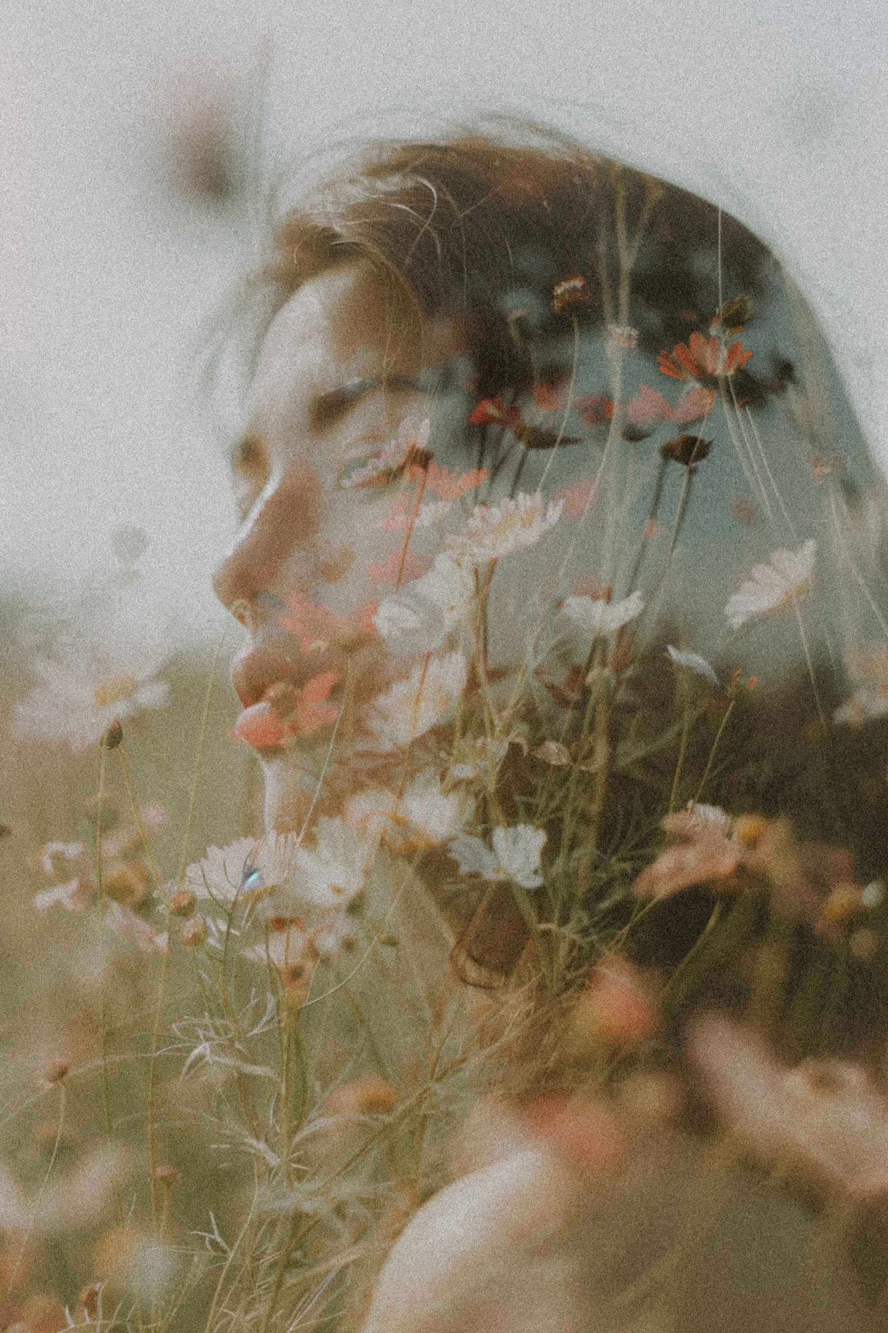 A woman with short brown hair and closed eyes, surrounded by a double exposure of flowers and grass.