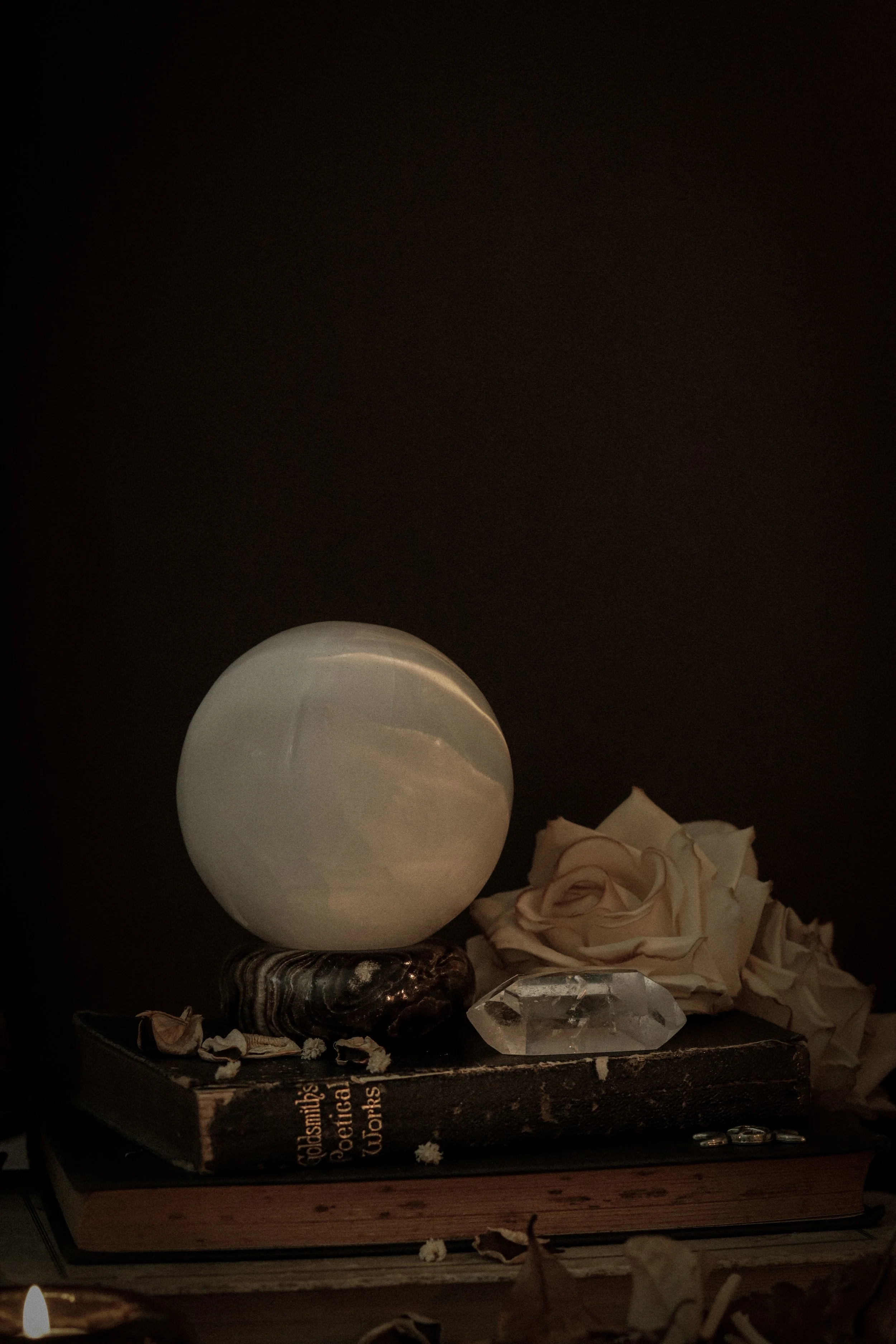 A decorative shelf display with a white spherical object, a black and white object, a crystal, and crumpled paper scattered around, with a candle in the foreground.