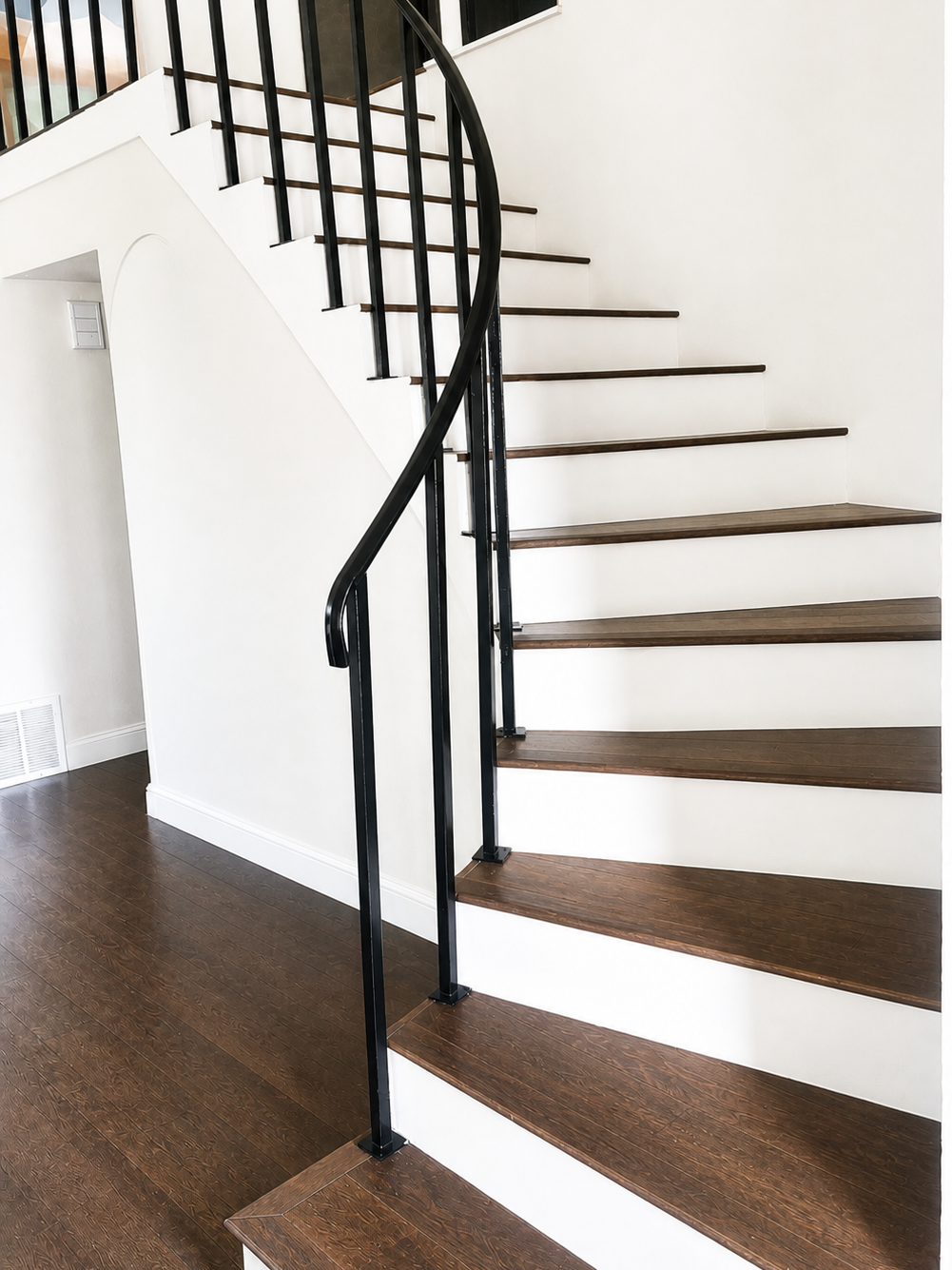 Interior view of a curved staircase with dark wooden steps and a black metal railing in a modern home.