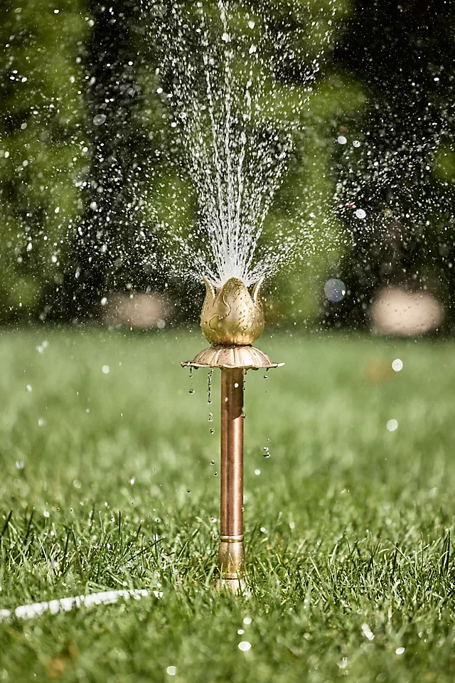 A garden sprinkler spraying water over grass with blurred trees in the background.