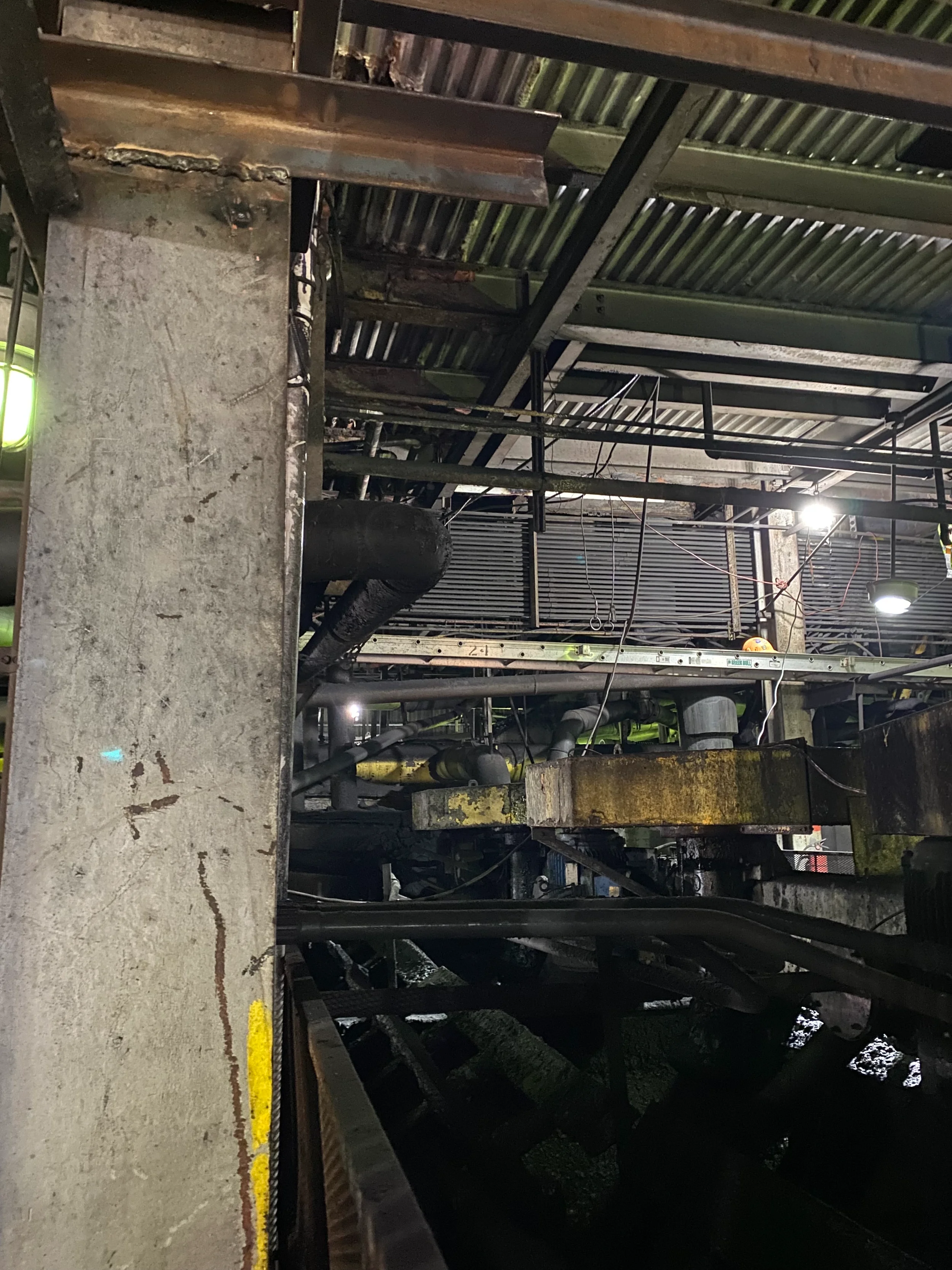 Industrial setting with metal stairs, pipes, scaffolding, and lighting, with concrete and metal surfaces.