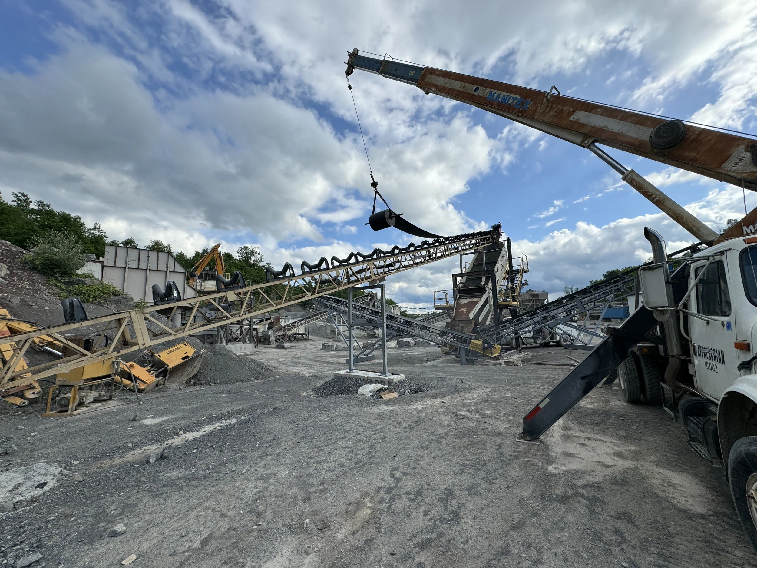 Construction site with cranes, conveyor belts, and construction equipment under a partly cloudy sky.