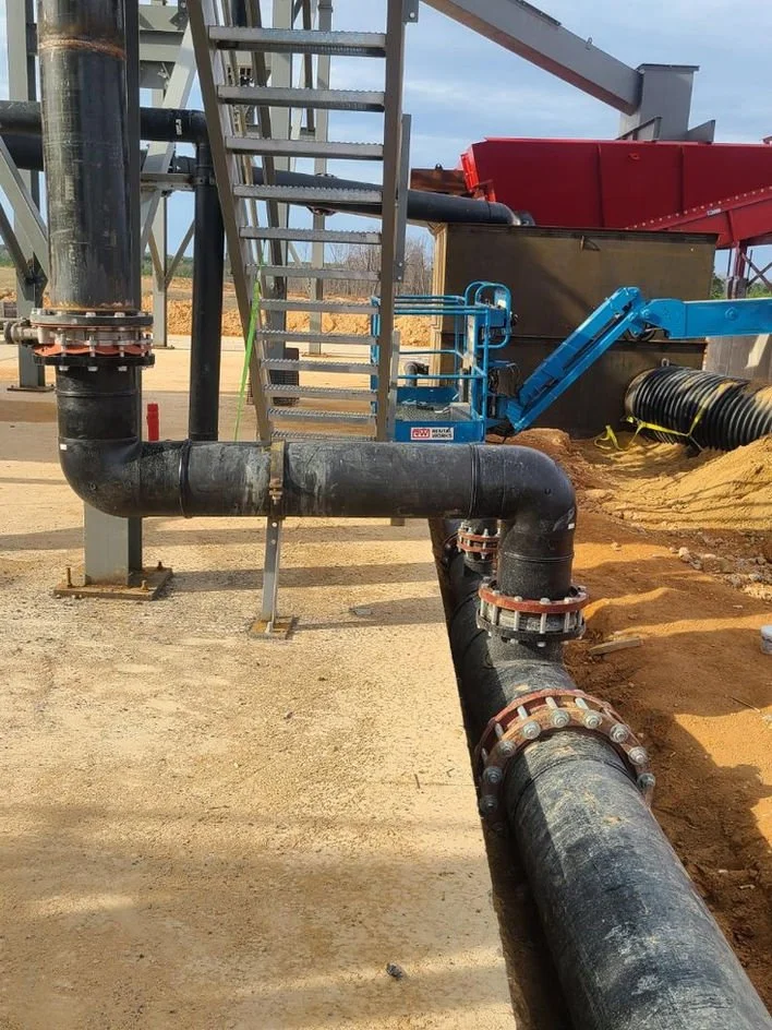 Underground piping and a blue mechanical device on a construction site with gravel and dirt.