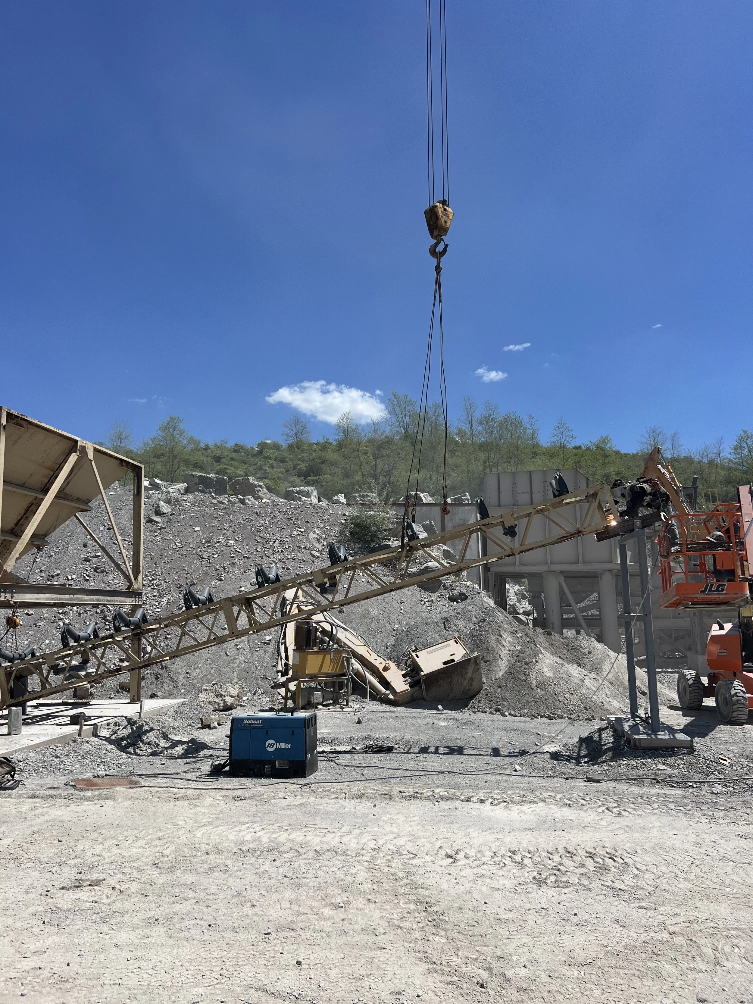 Construction site with heavy machinery, including a crane lifting a large object, and construction equipment, under a blue sky with a few clouds.