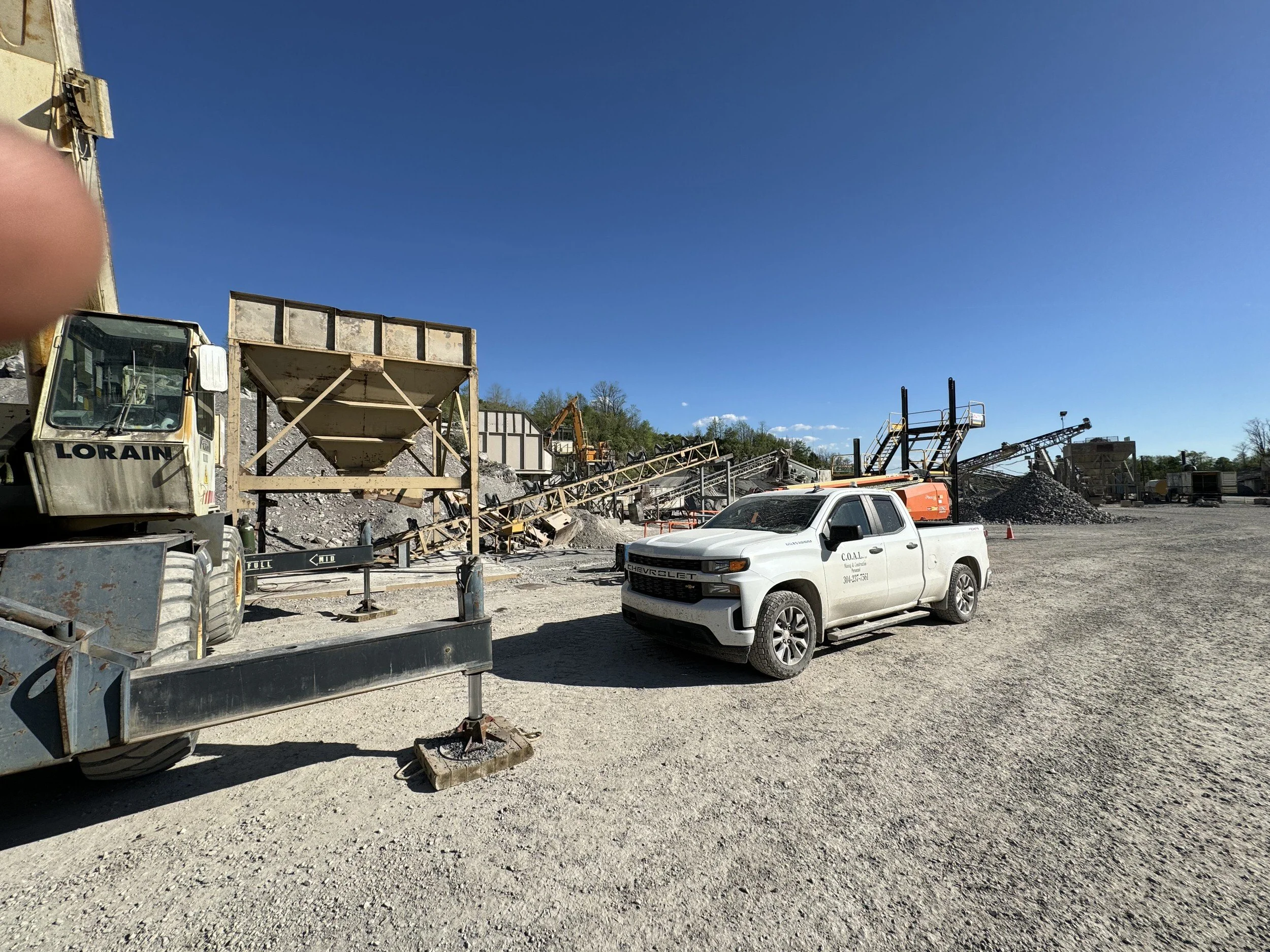 Construction site with heavy machinery, gravel piles, a white pickup truck, and a clear blue sky.