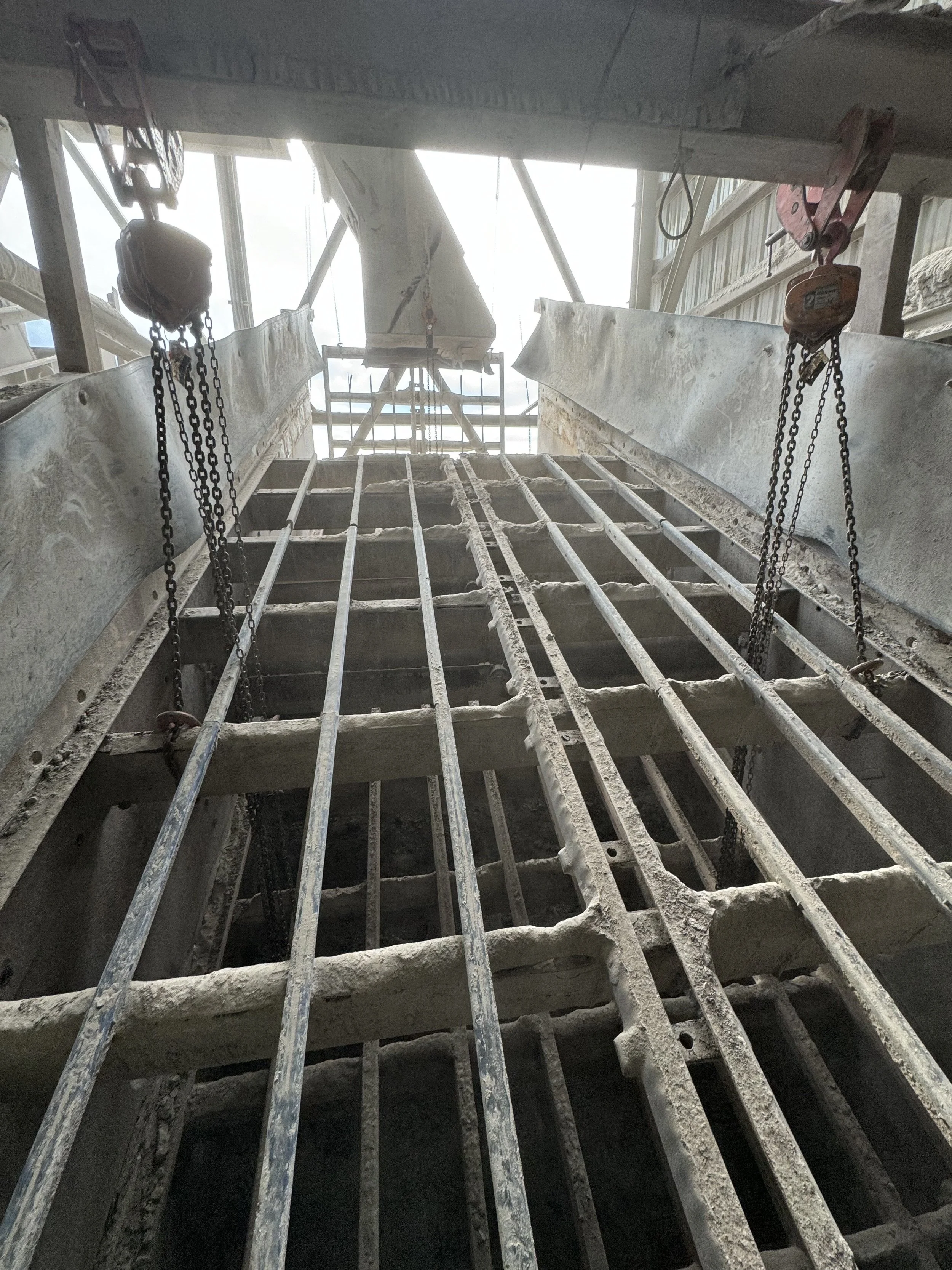 Under construction site with metal scaffolding, hoists, and beams, looking upwards toward the sky.