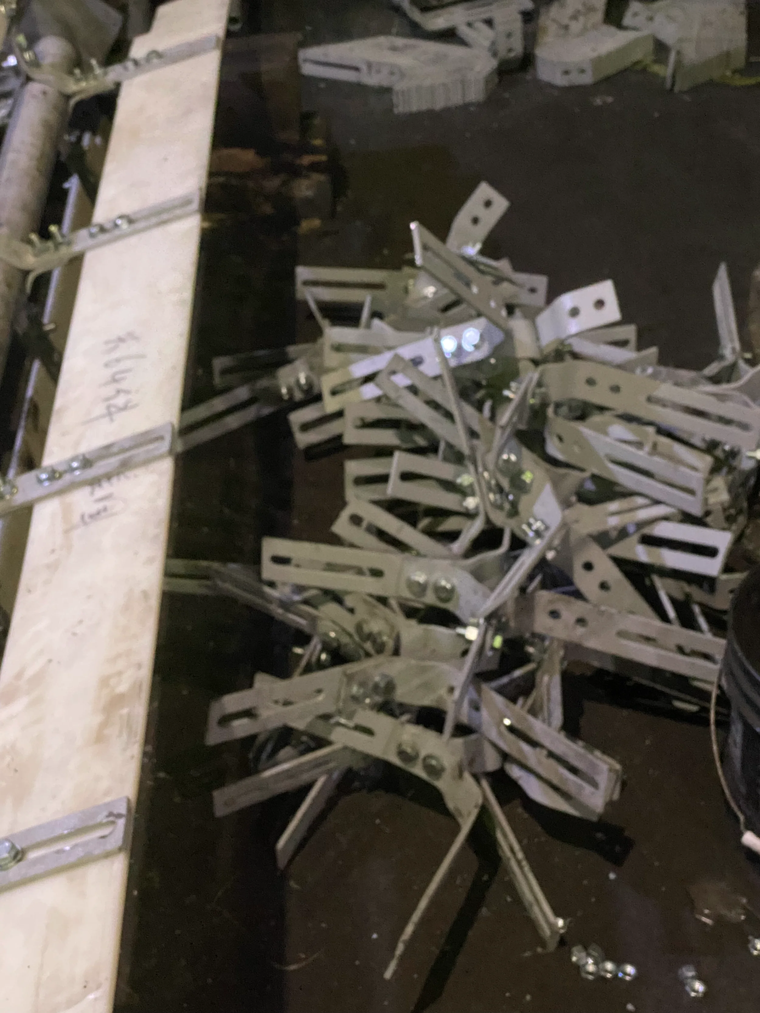 Photo of a pile of disorganized metallic items and tools on a dark surface, with a wooden plank on the left side.