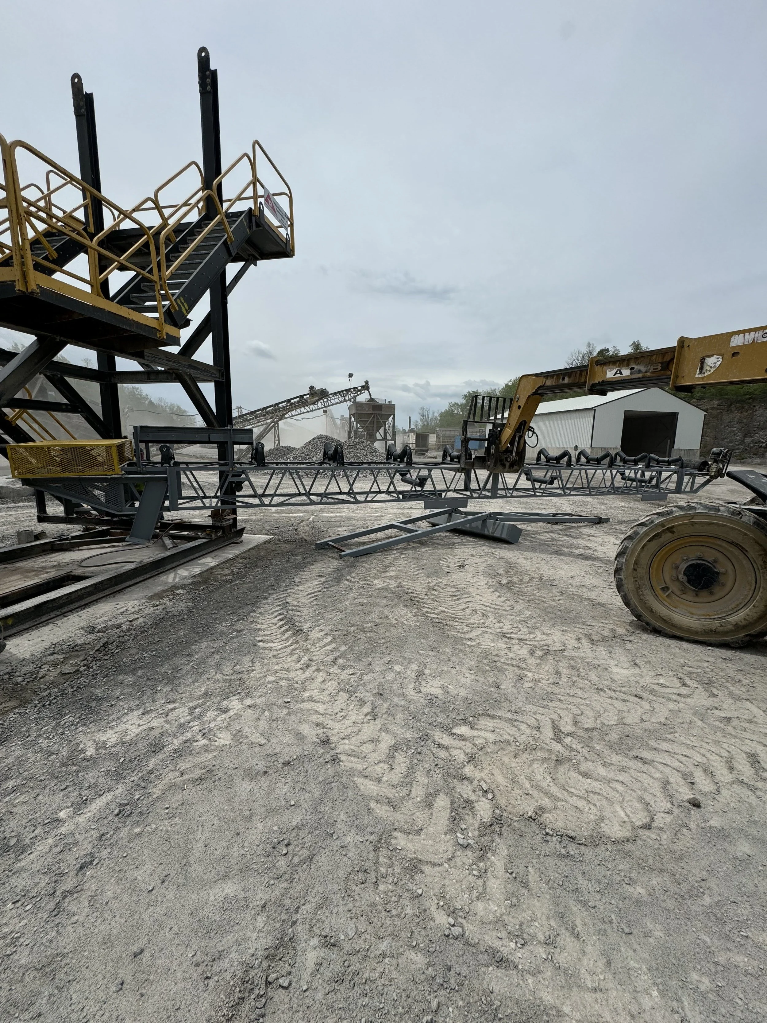 Construction site with machinery and equipment for gravel or rock processing, on a dirt ground under an overcast sky.