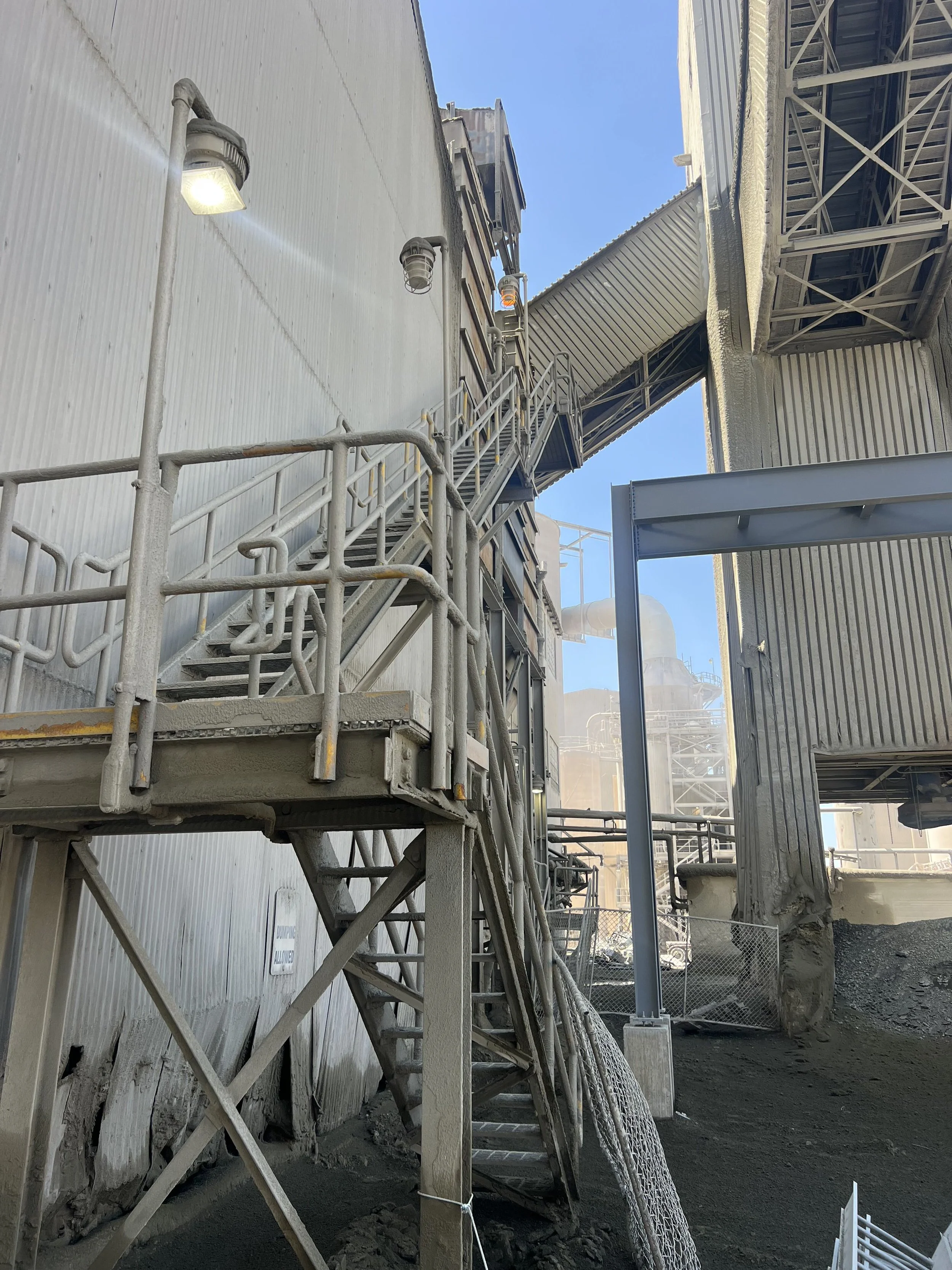 Industrial building with metal stairs, multiple pipes, and walkways, under clear blue sky.