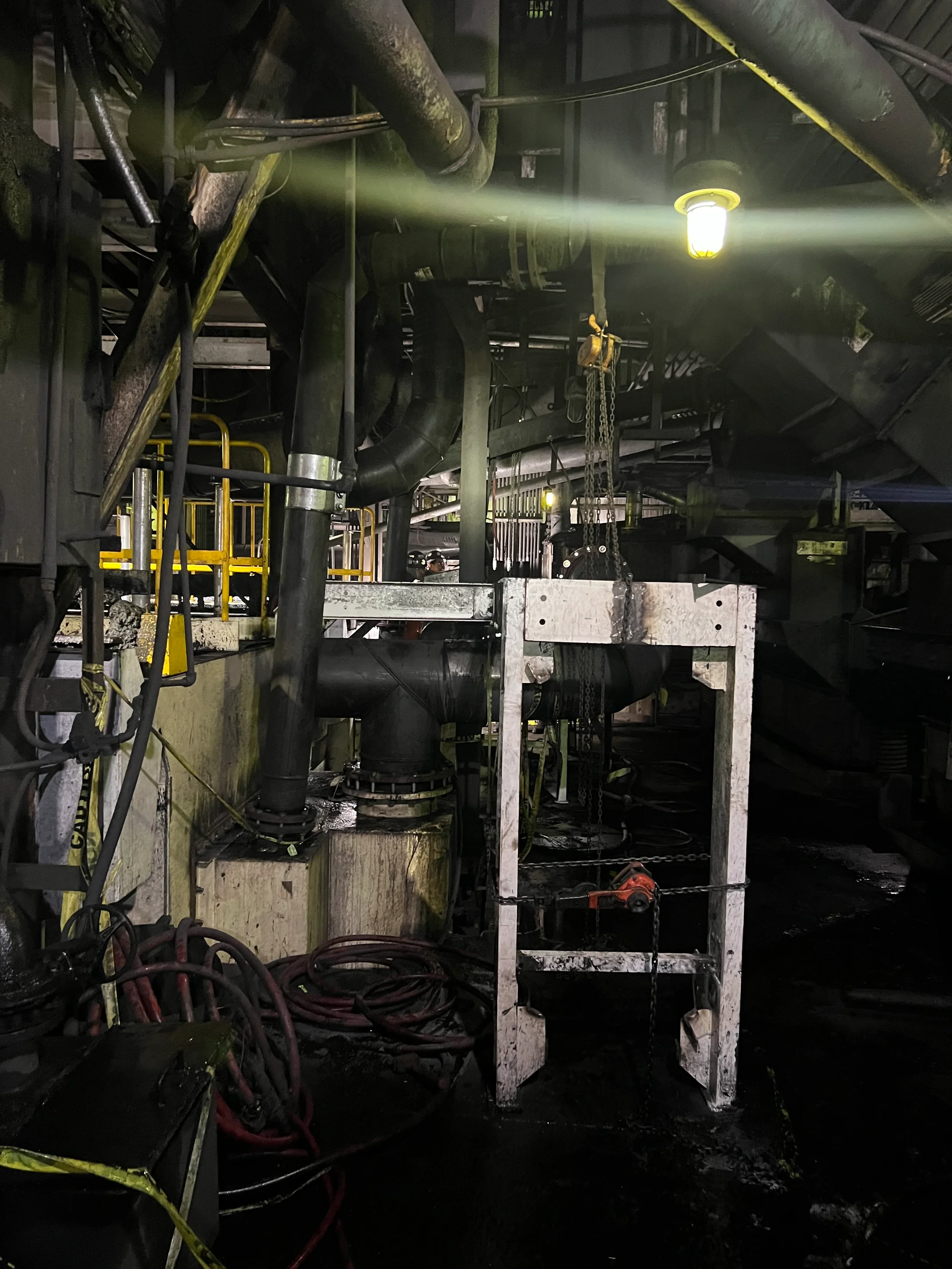 Interior of industrial facility or factory with pipes, cables, chains, and a bright light fixture