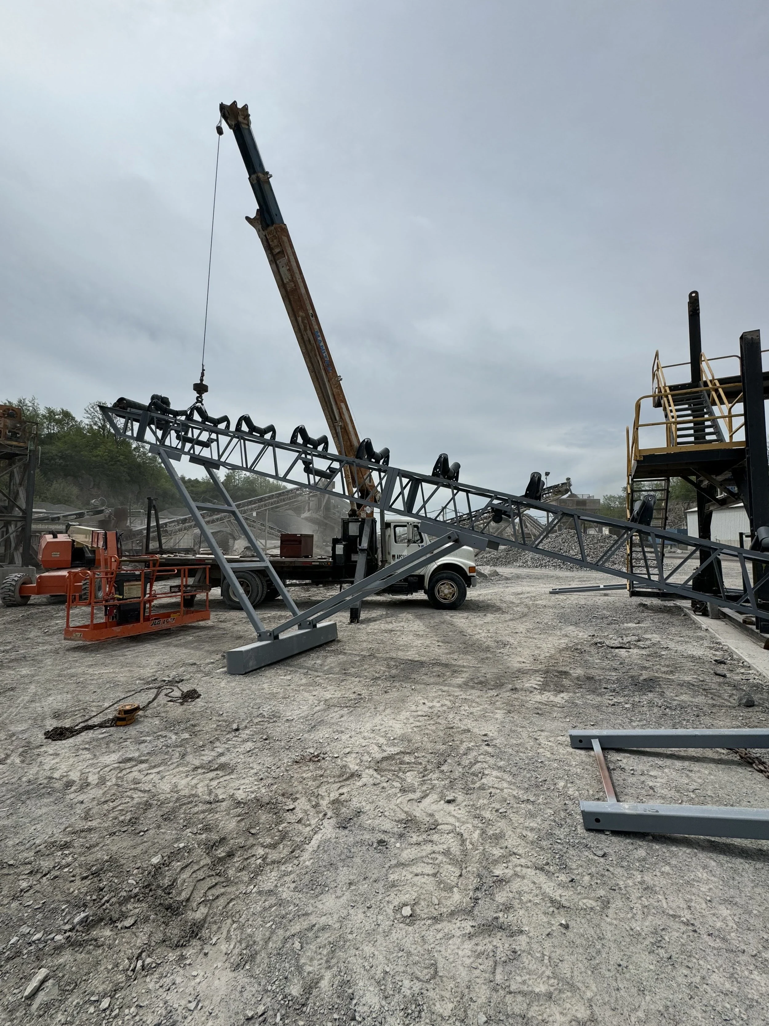 Construction site with crane, metal framework, equipment, and stairs, on a cloudy day.