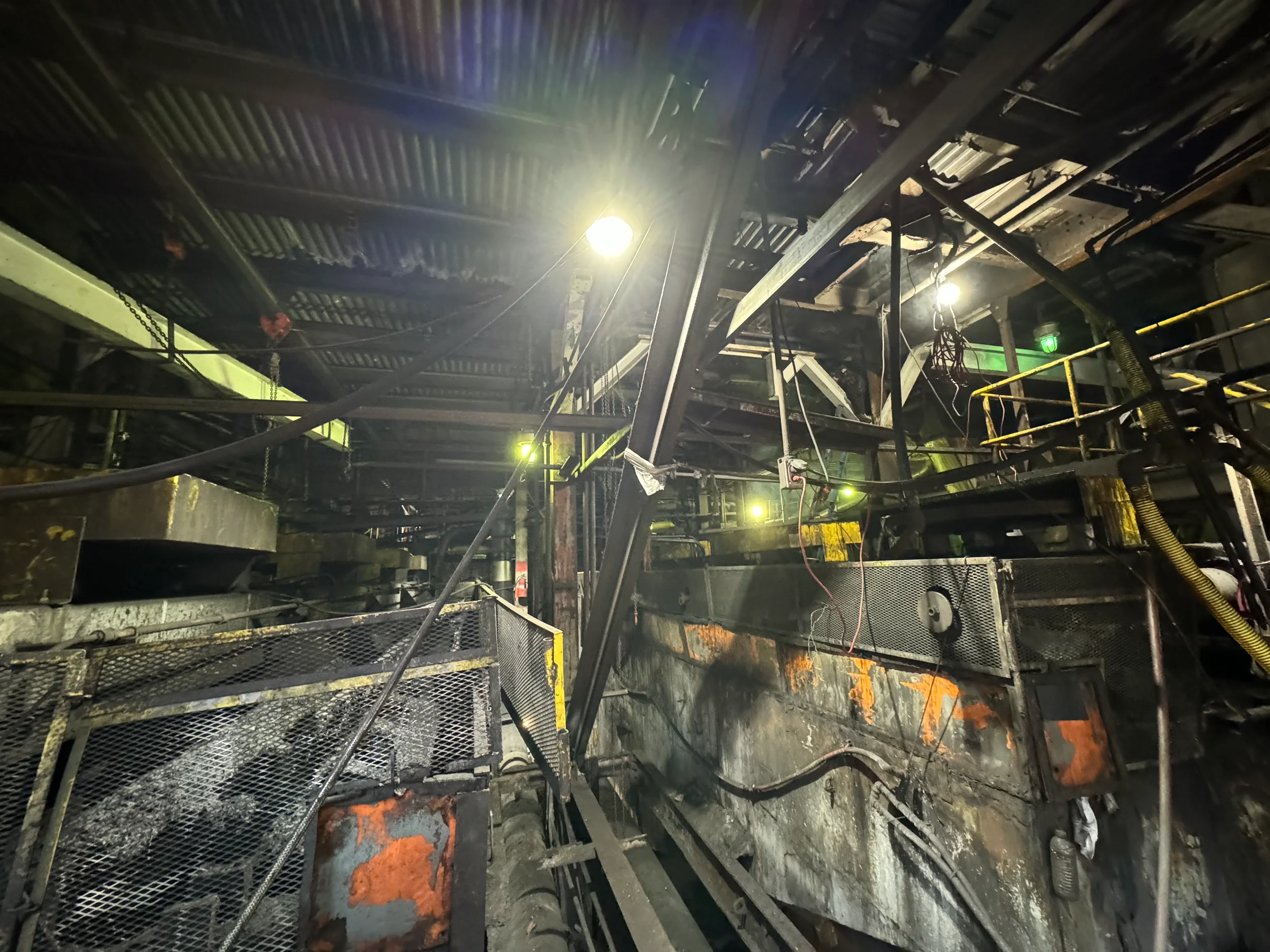 Industrial interior with metal scaffolding, pipes, and equipment, under bright lights, showing signs of fire or heat damage.