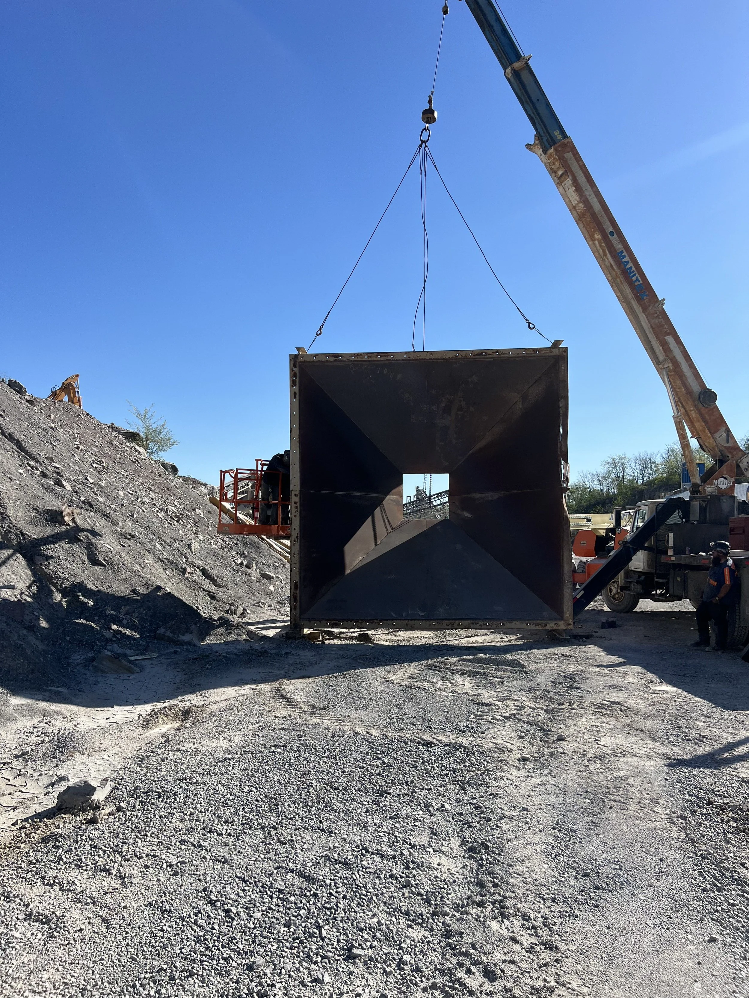 A large crane lifting a rectangular metal structure at a construction site on a clear day.