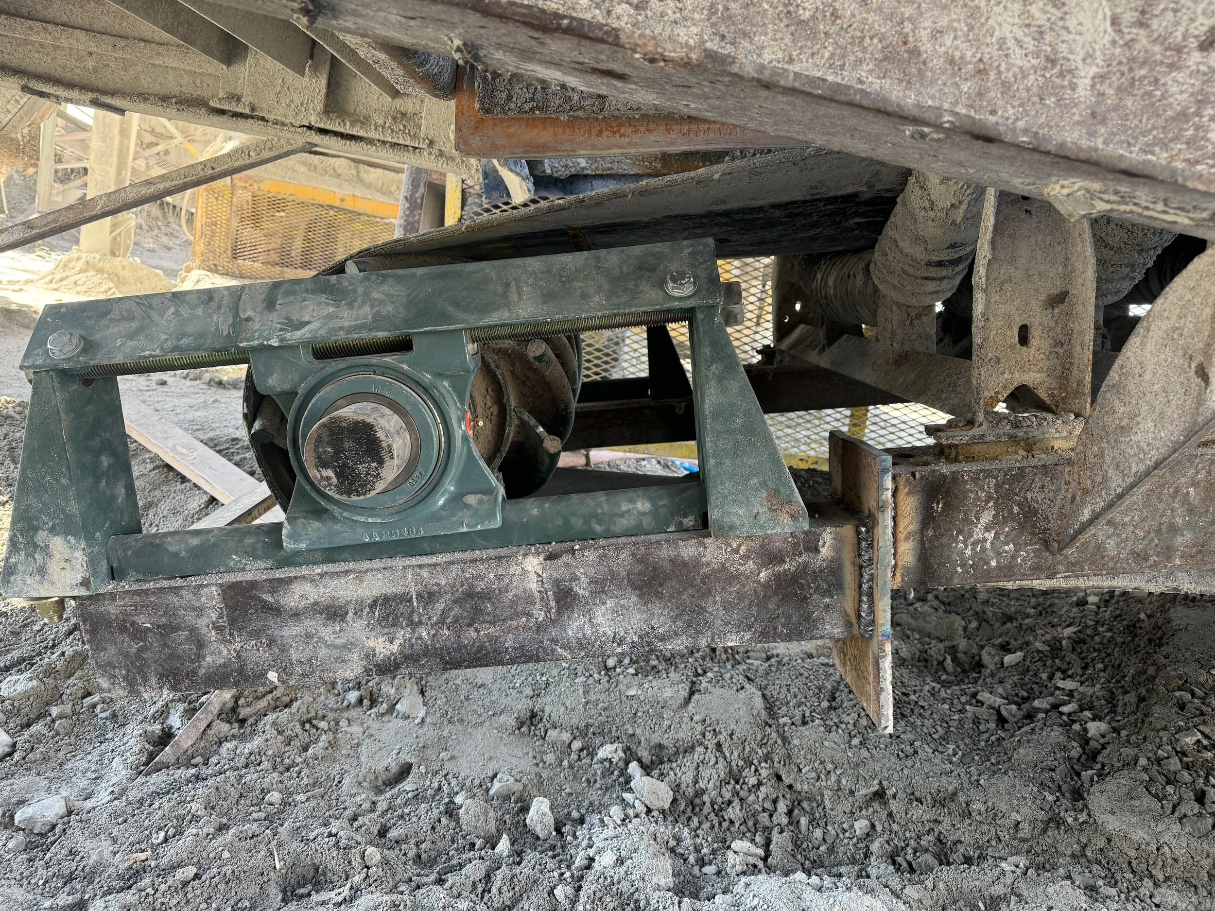 Close-up of construction equipment on dirt ground showing a metal frame, bolts, a rotating part, and surrounding dirt and debris at a construction site.