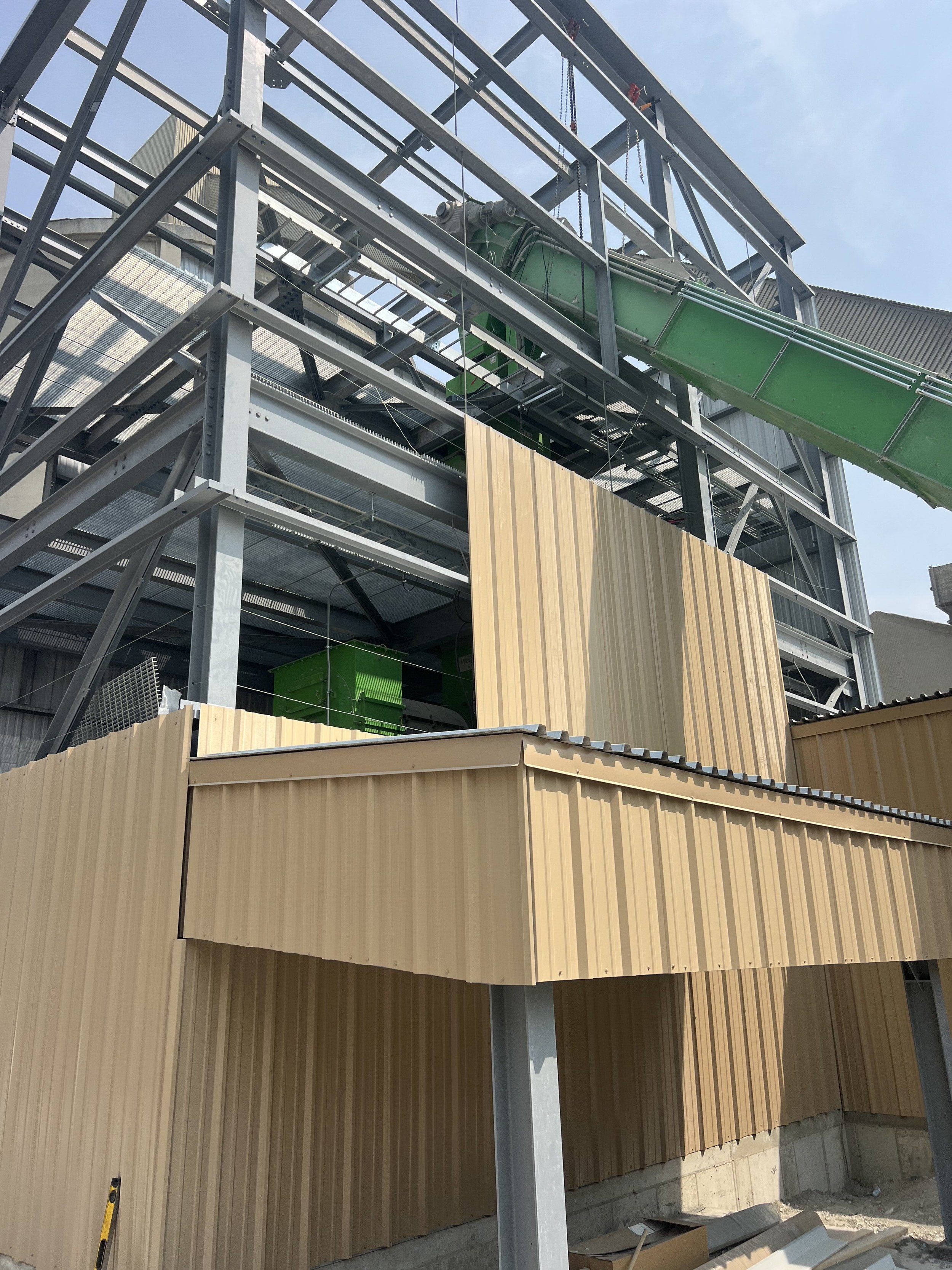 Construction site with metal framework, green slide structure, and beige wood paneling on a building under construction.